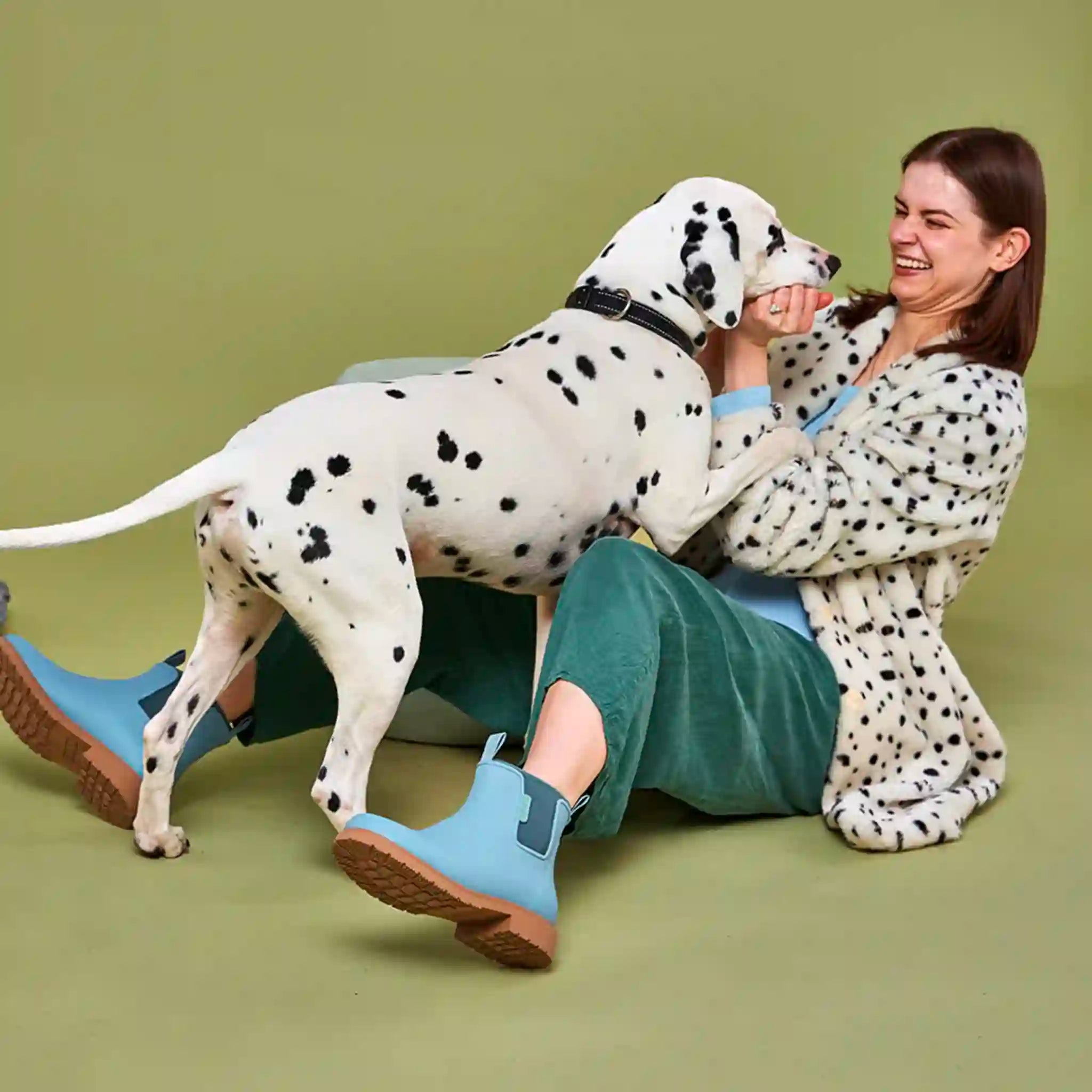 Woman in a polka dot robe playing with a Dalmatian dog on a green background