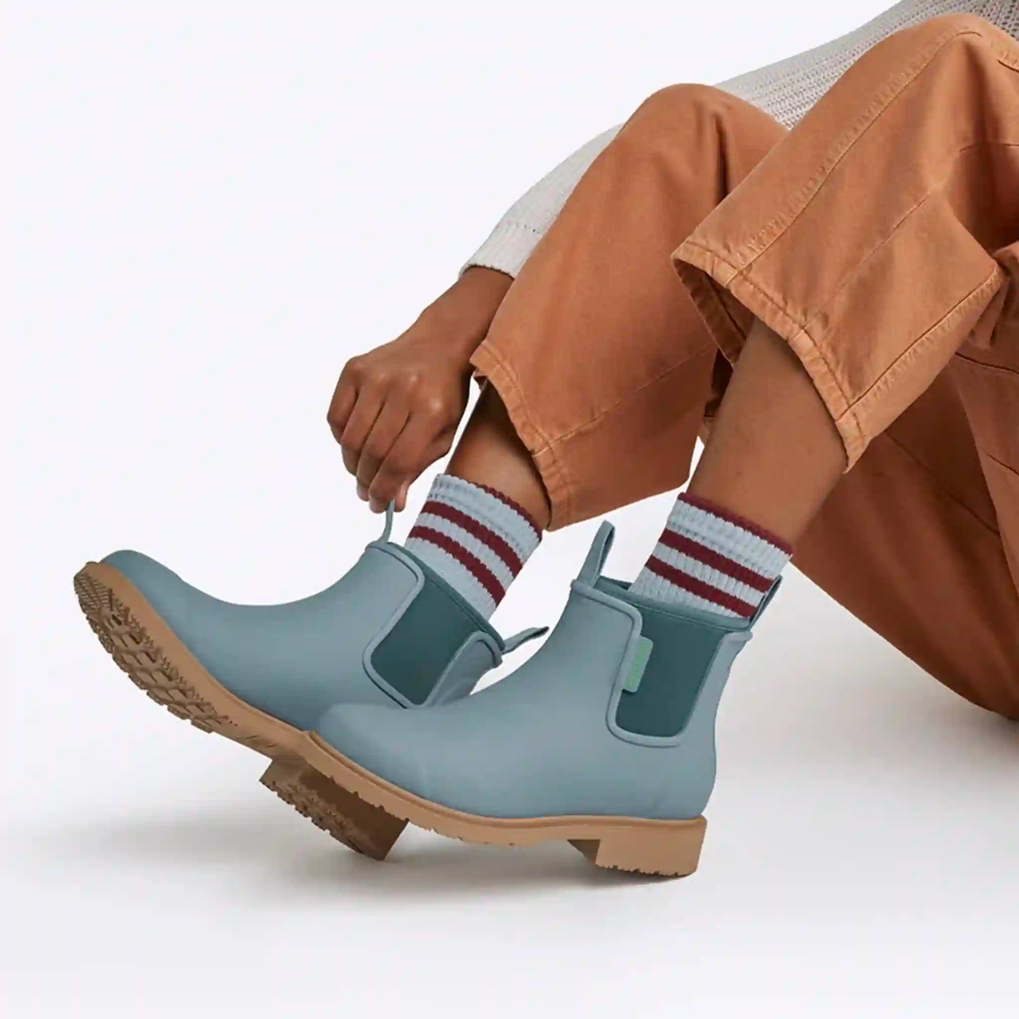 Person wearing light blue rubber boots with brown soles on a white background