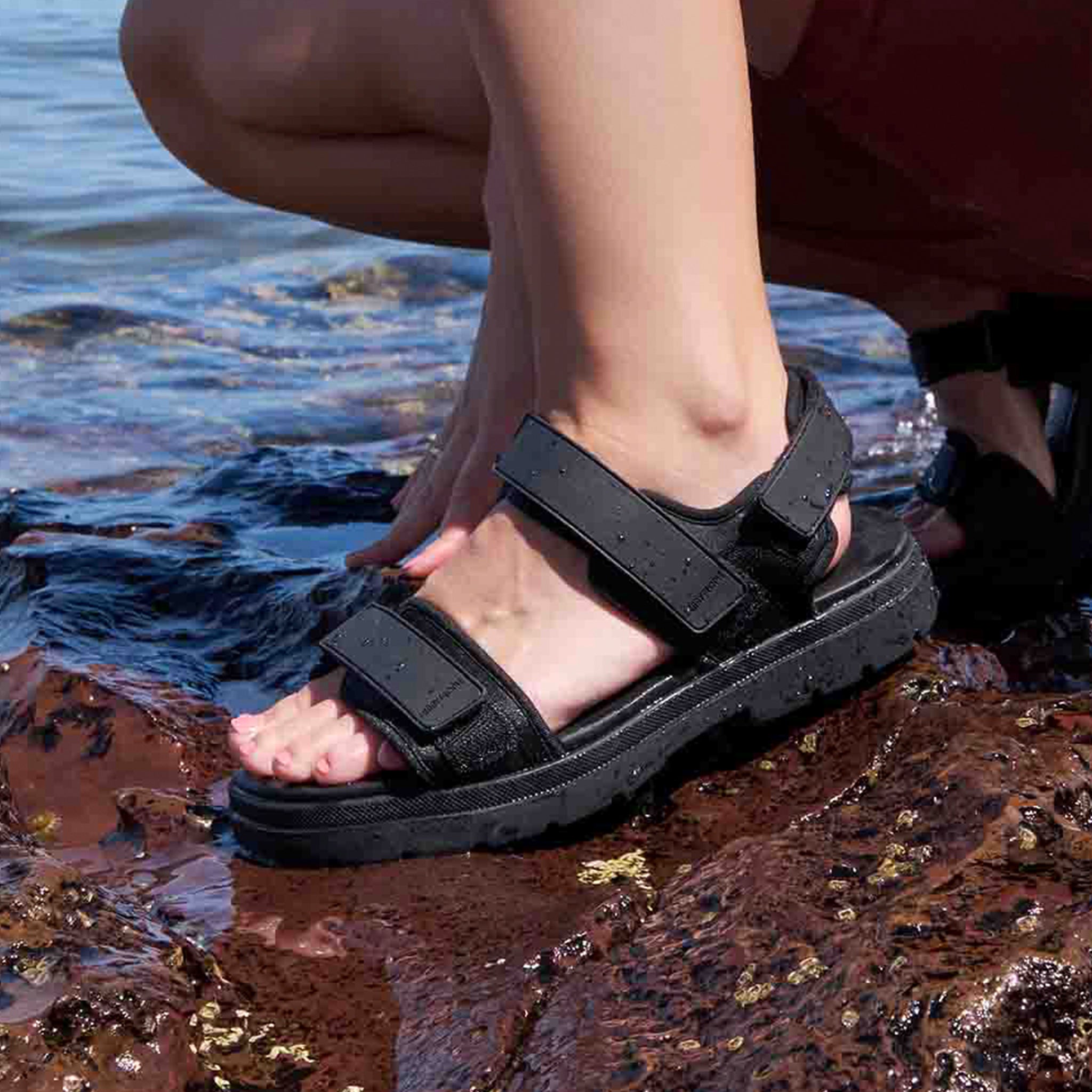 Person wearing black sandals by a body of water