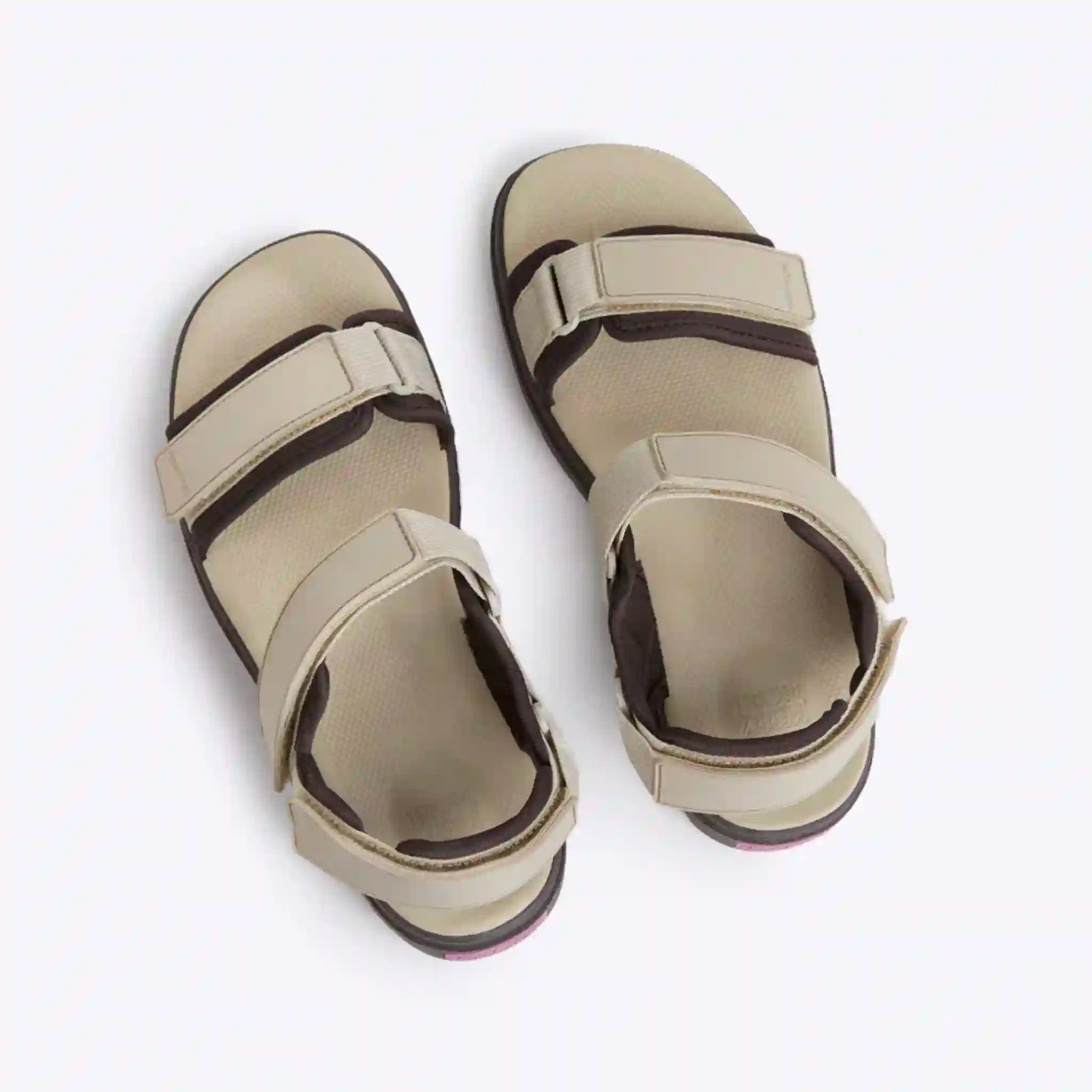 Pair of beige sandals with black straps on a white background
