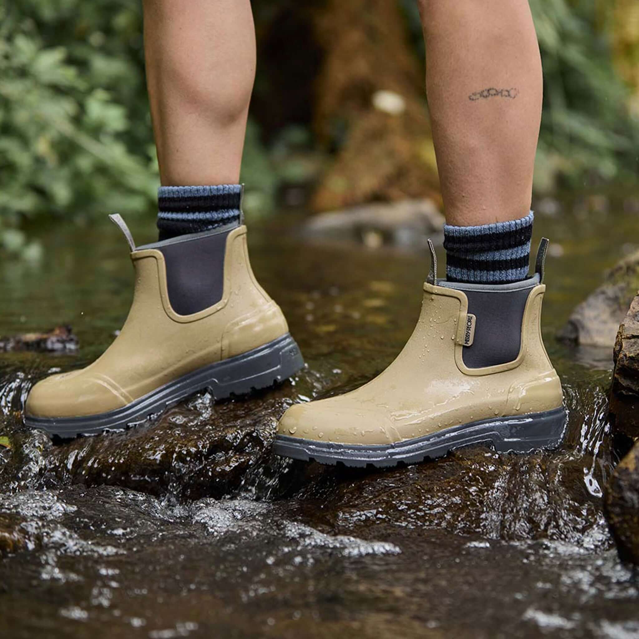 Alt Tag: Merry People Oberon Boots - Stone waterproof natural rubber ankle boots worn in a rocky creek, unisex wide-fit comfort