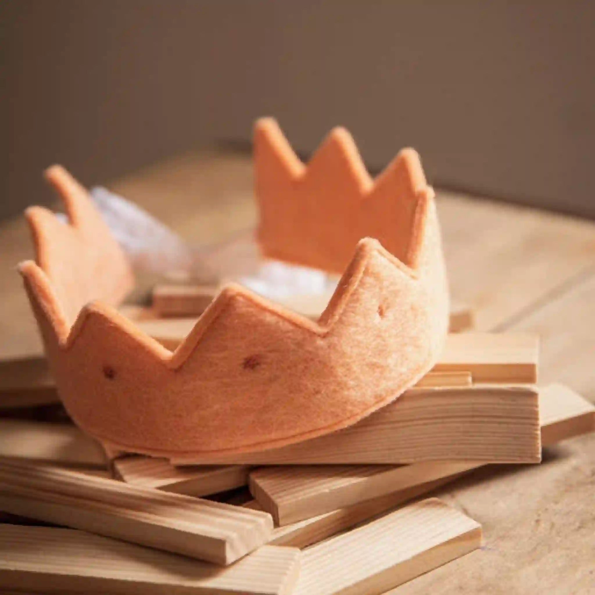 A orange felt crown with gold stars and a cotton ribbon for tying, suitable for children and adults.