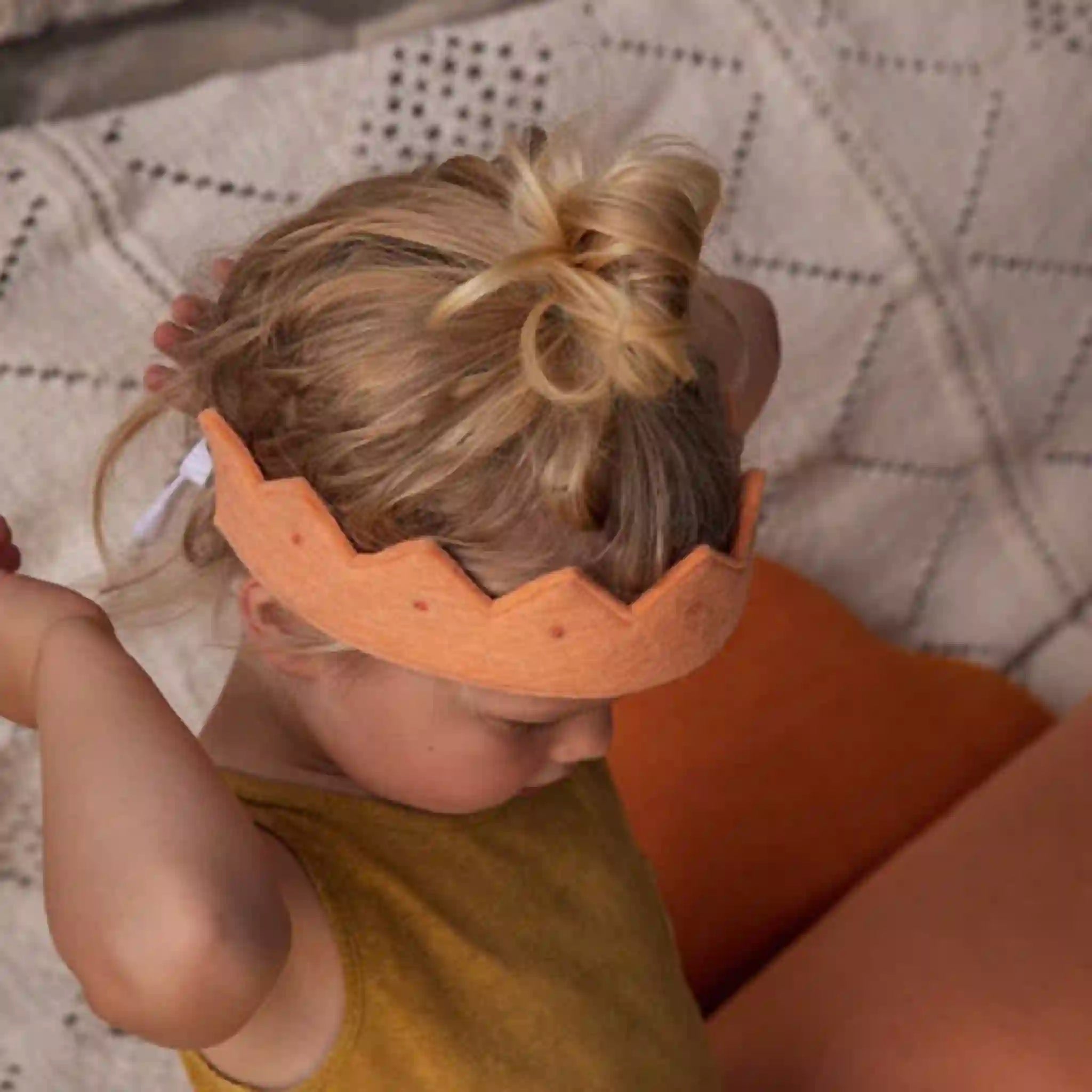 Child wearing a wooden headband with a textured blanket in the background
