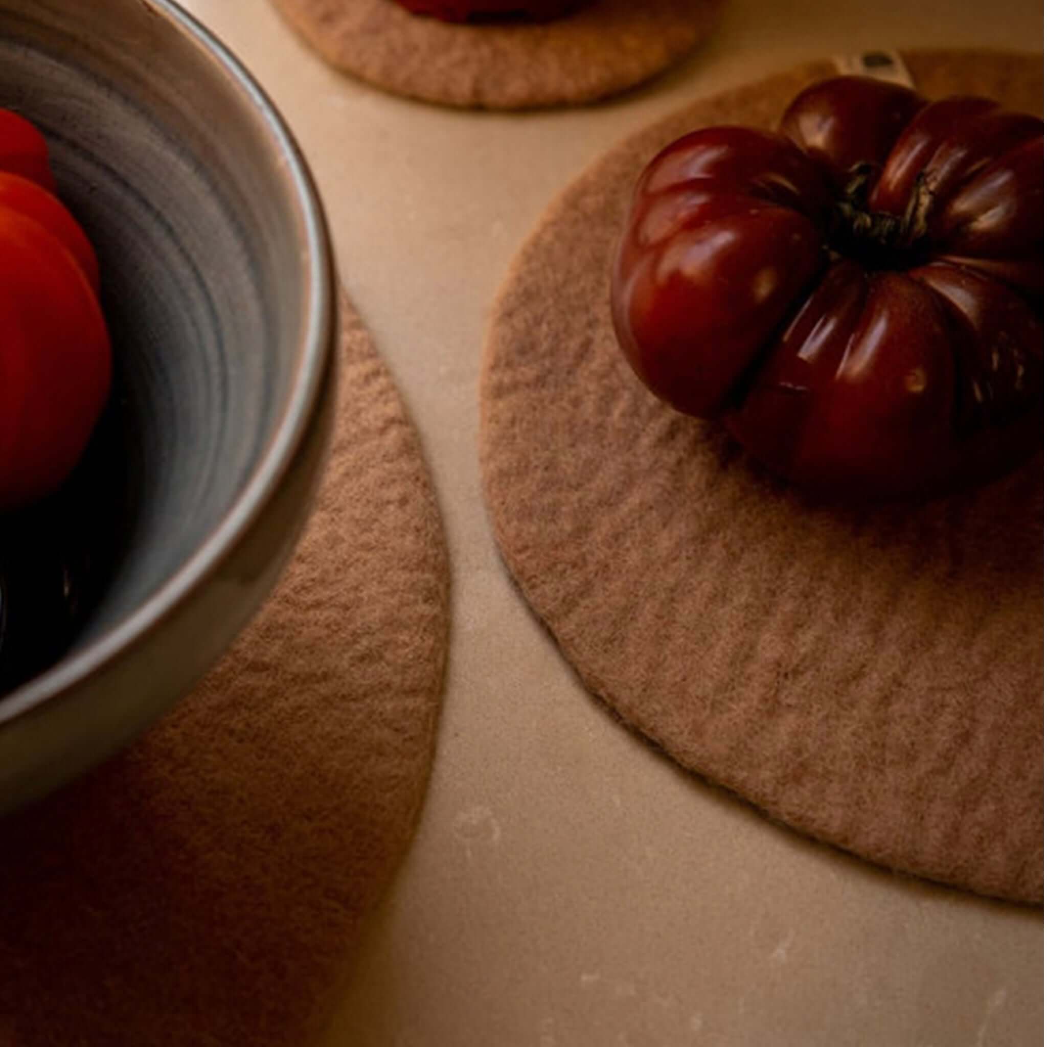 Muskhane Felt Plain Round Coaster - Nude in use with bowl and tomatoes, showcasing its design and color.