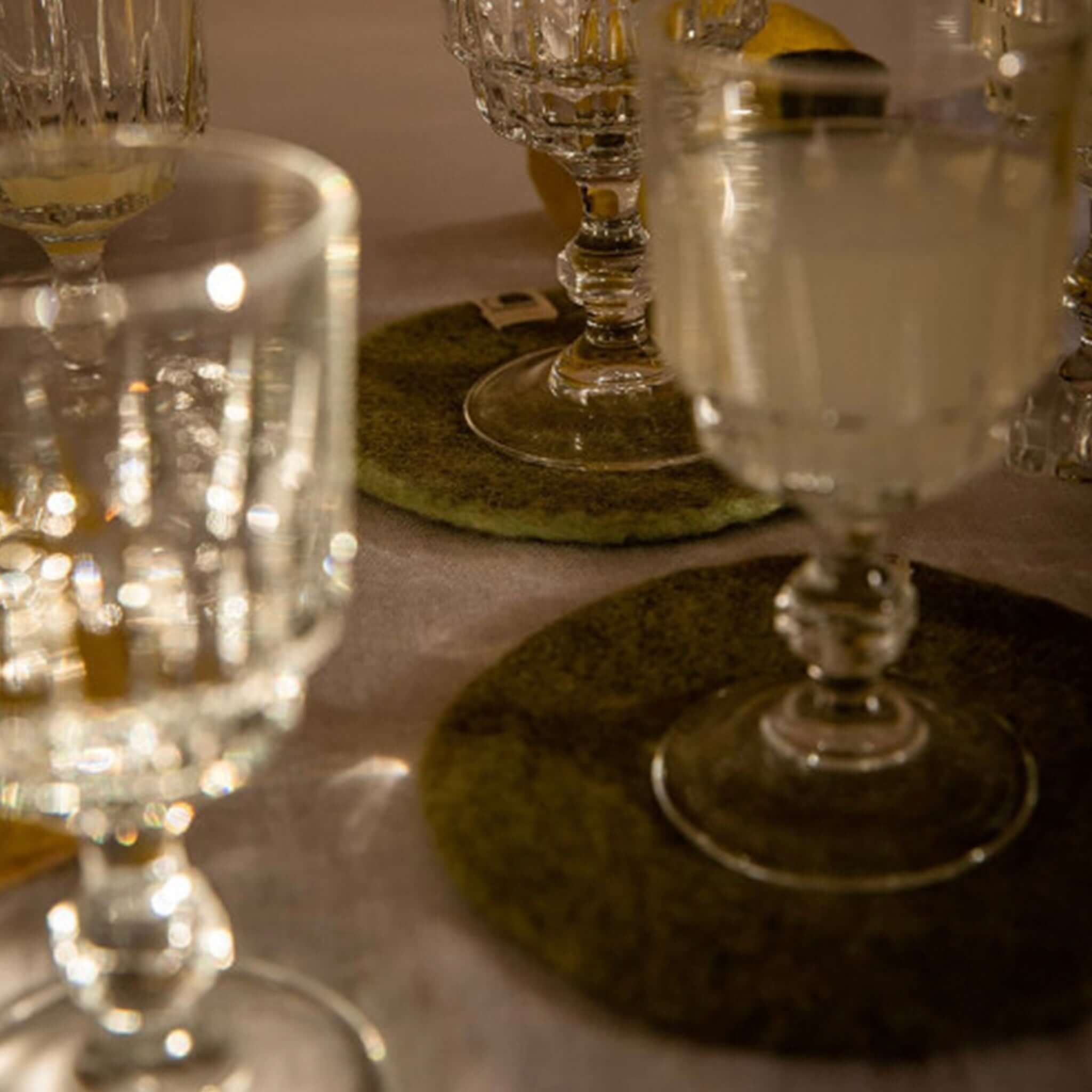 Muskhane Felt Plain Round Coaster - Sage under elegant glassware on a beautifully set table.