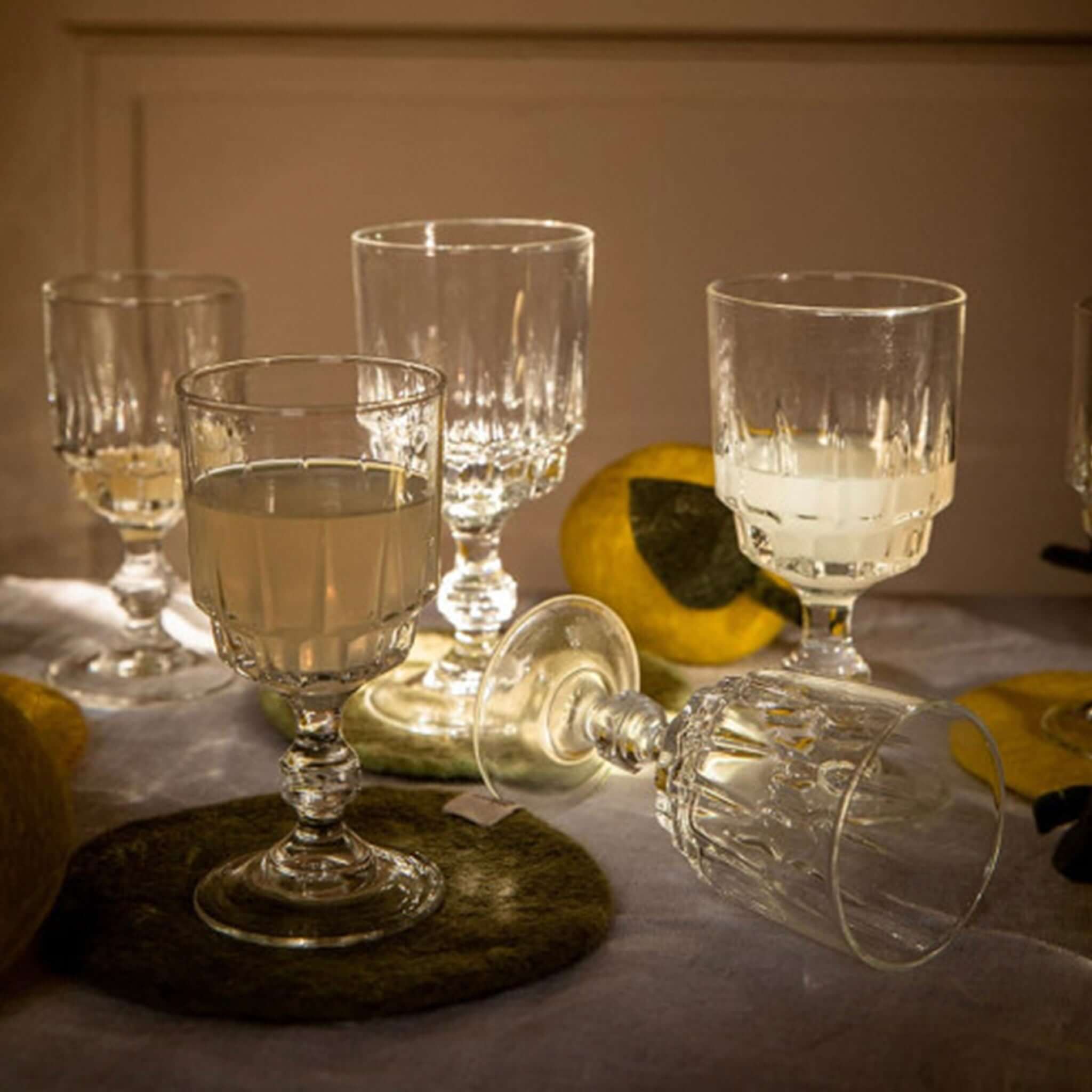 Muskhane Felt Plain Round Coaster - Sage with elegant glassware and lemon decor in a soft-lit setting.