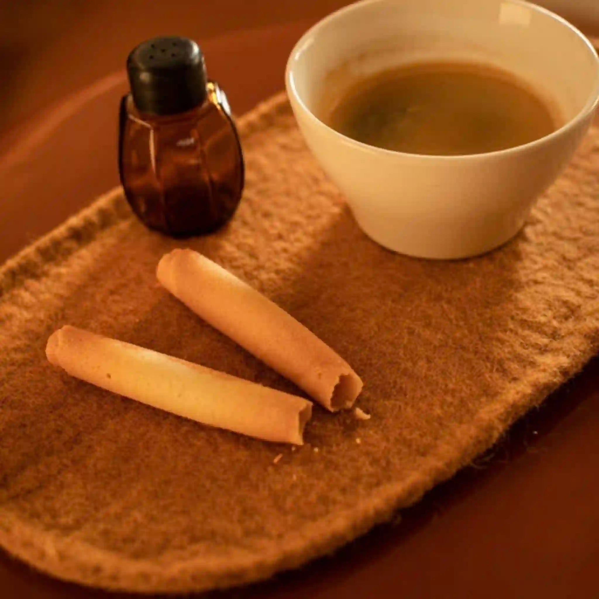 White bowl with brown liquid, two rolled-up items, and a small bottle on a textured surface.