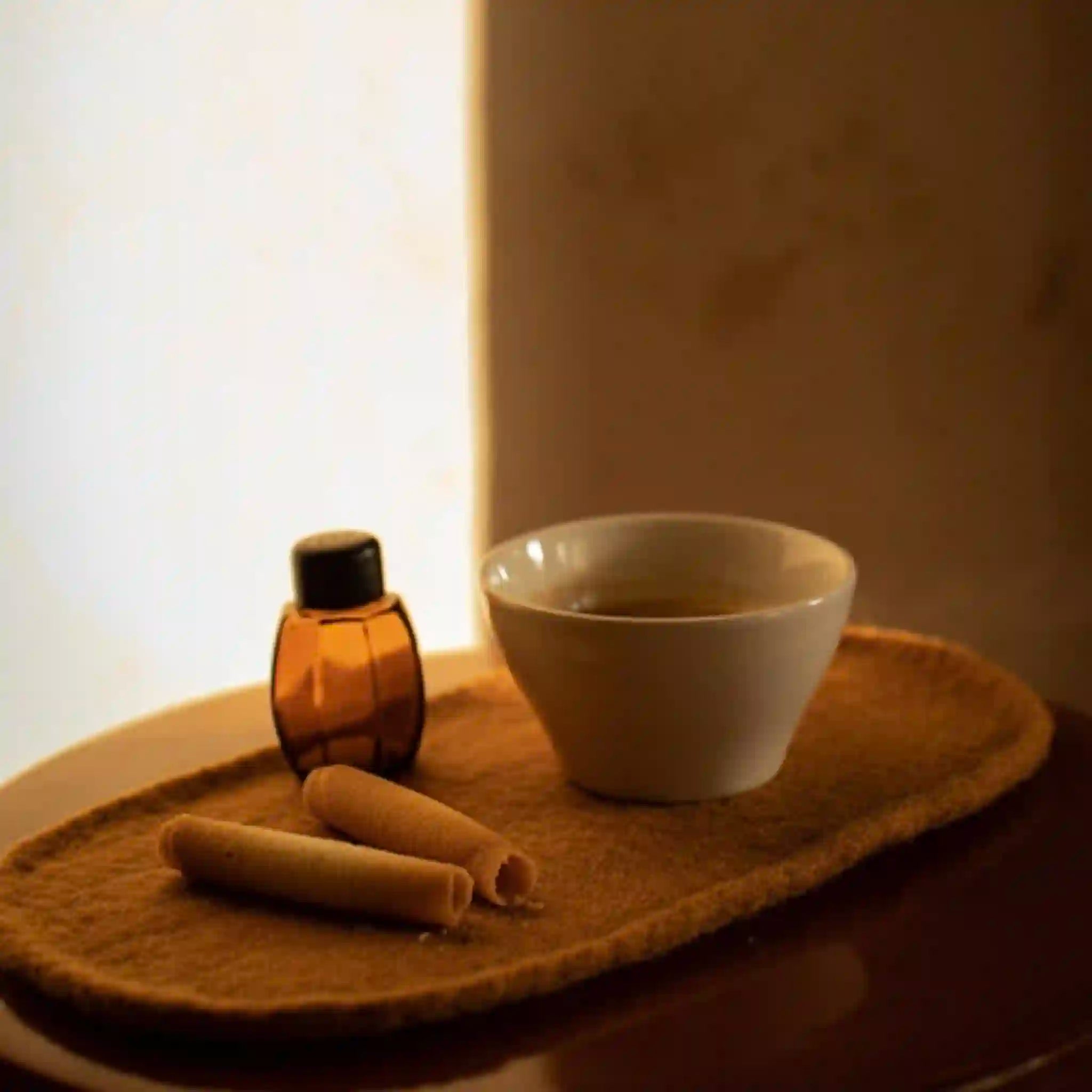 Small bottle, two cylindrical objects, and a white bowl on a textured surface with a blurred background.