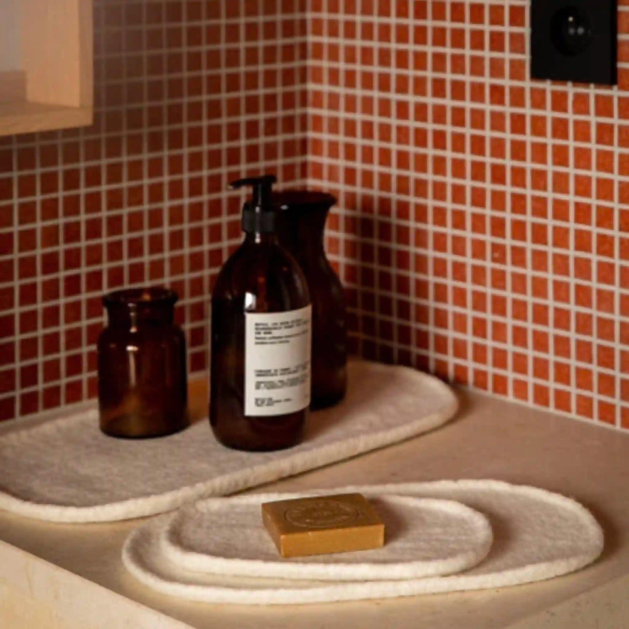 Bathroom setting with brown bottles, a soap bar, and a towel on a tiled wall background.
