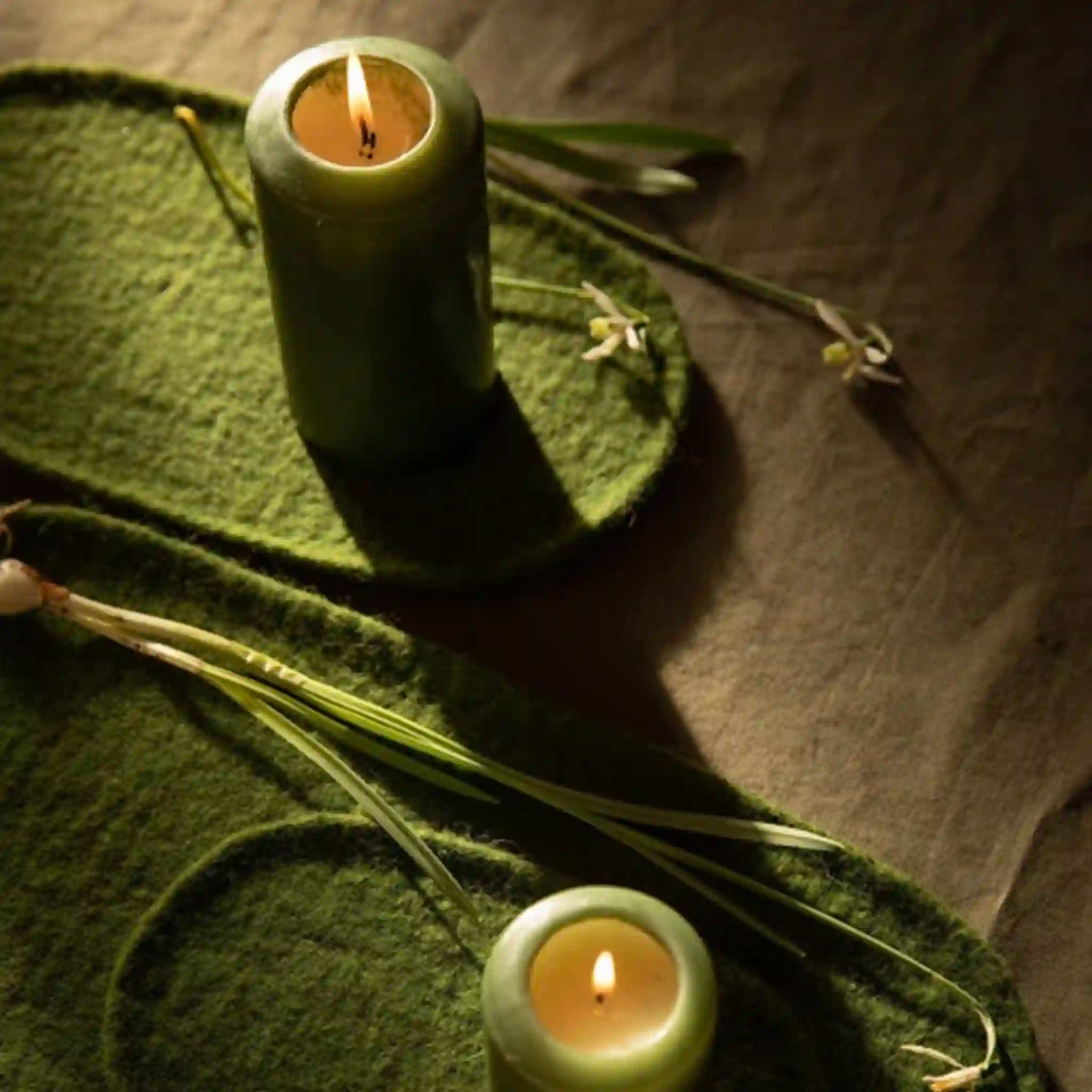 Two green candles on a textured surface with green leaves.