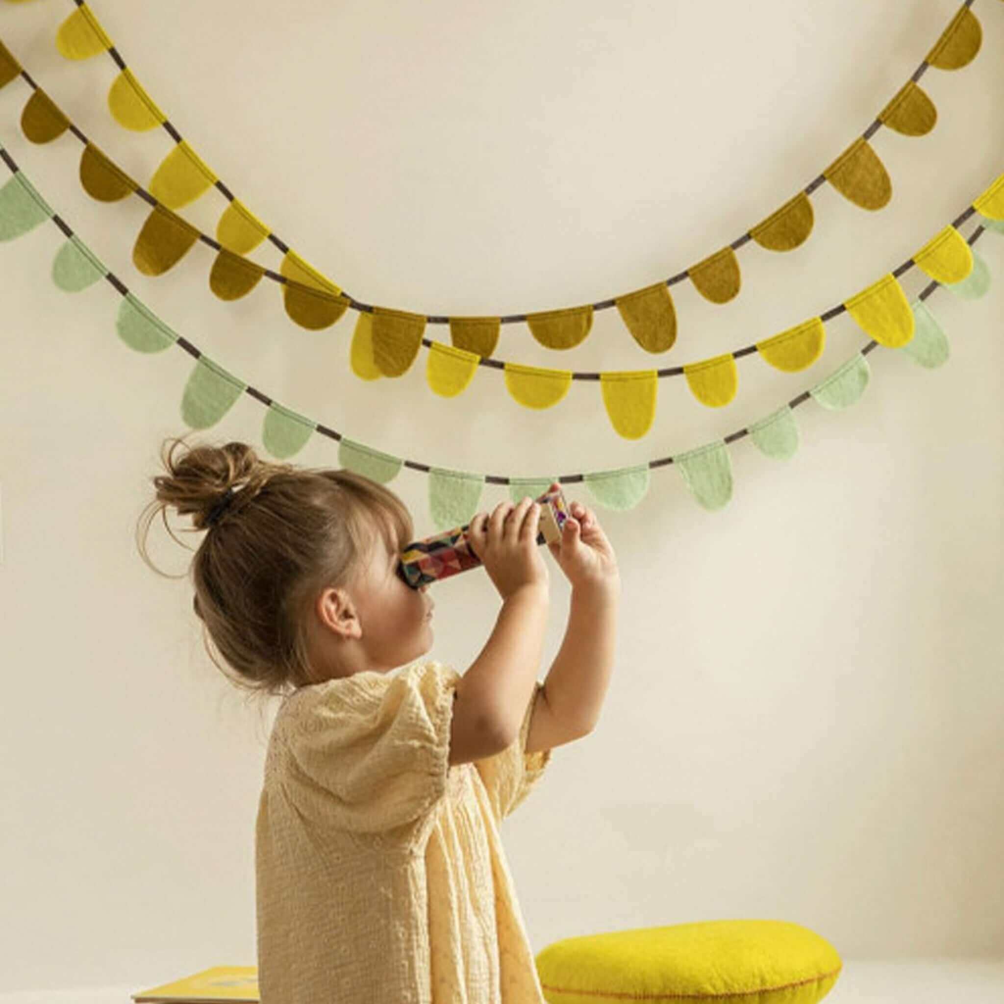 Child playing with a toy under the Muskhane Felt Round Flag Garland - Mint hanging on the wall.