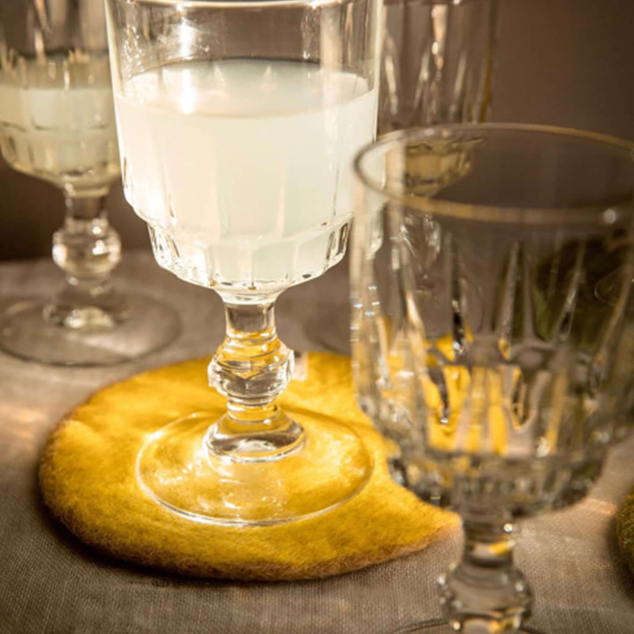 Muskhane Felt Two Tone Round Coaster - Nude & Lemon used under a glass on a table.