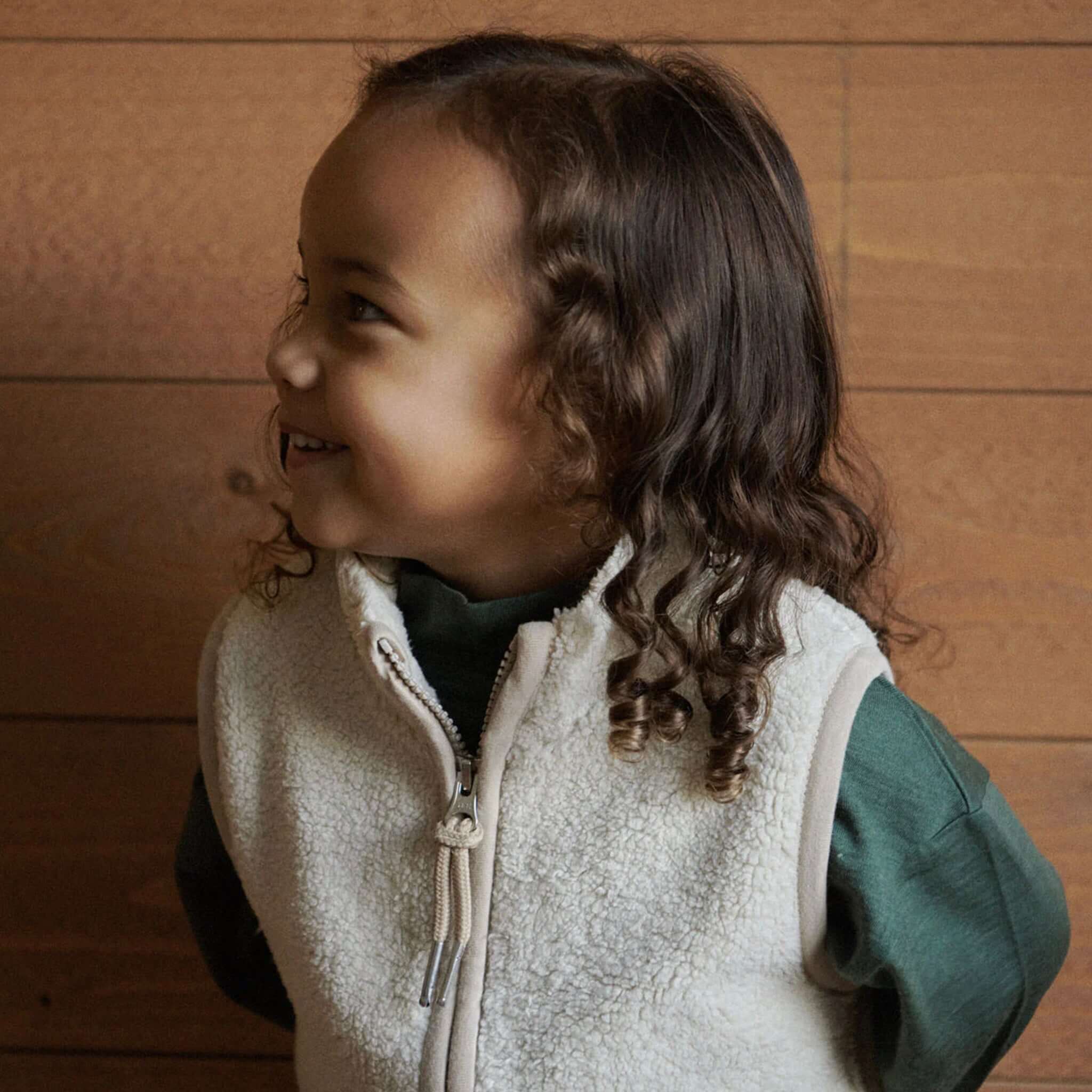 Alt Tag: Nature Baby Flint Vest - Oatmeal worn by child, cosy recycled polyester cream vest with YKK zip, high neck and patch pockets