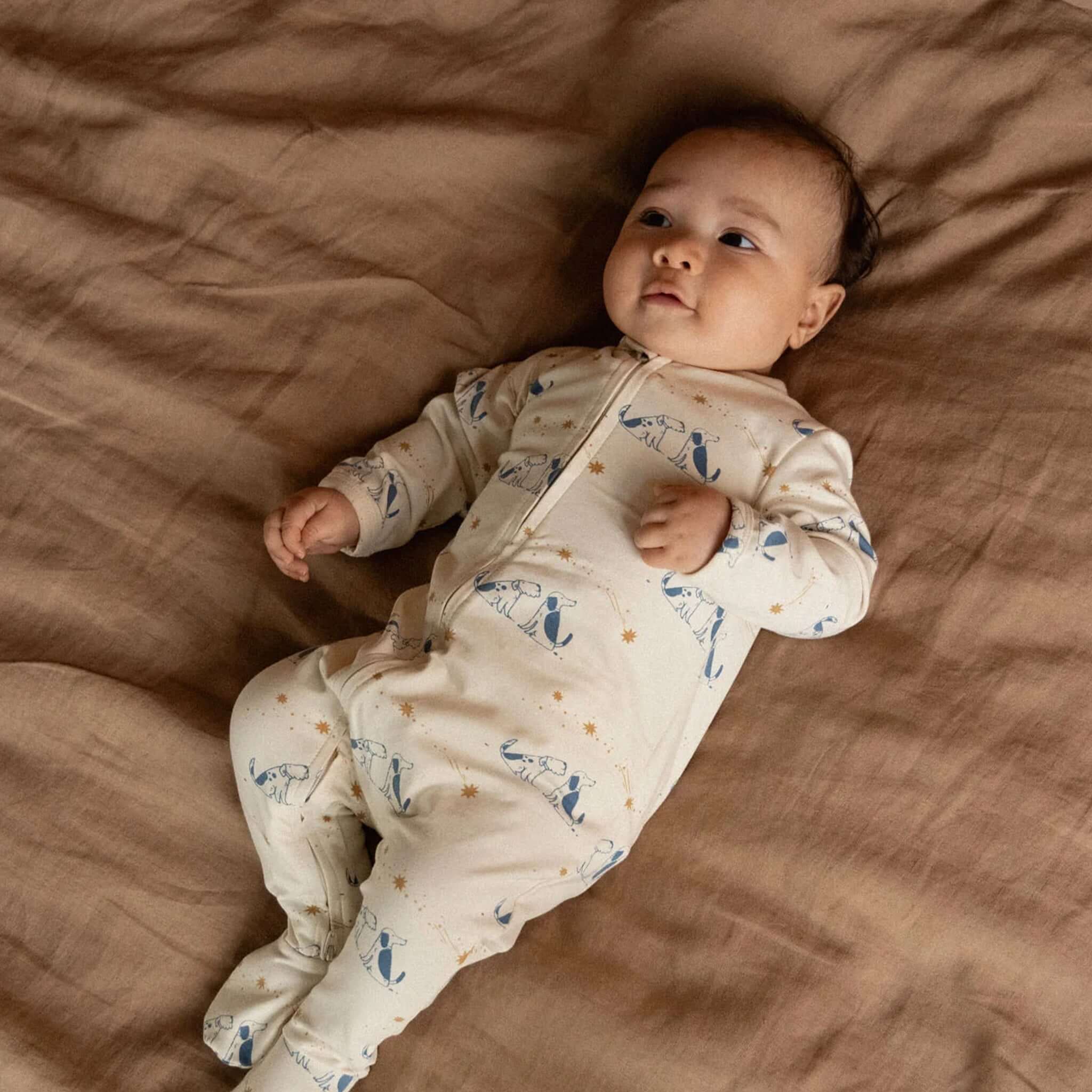Baby in Nature Baby Organic Cotton Dreamlands Suit - Dog Dream, lying on a bed with a serene expression.