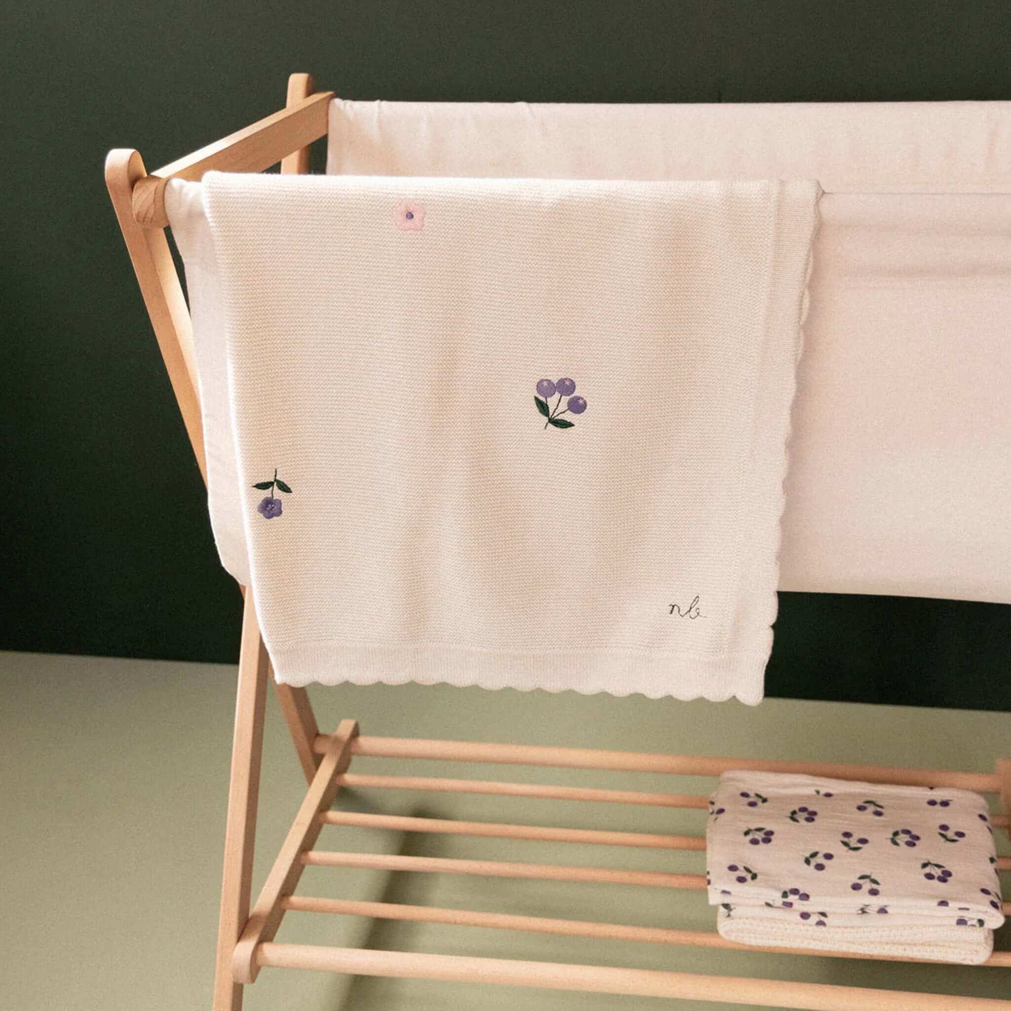 Alt Tag: Nature Baby Organic Cotton Fern Blanket - Berry Garden organic cotton knit baby blanket with floral embroidery and scalloped edge on wooden rack