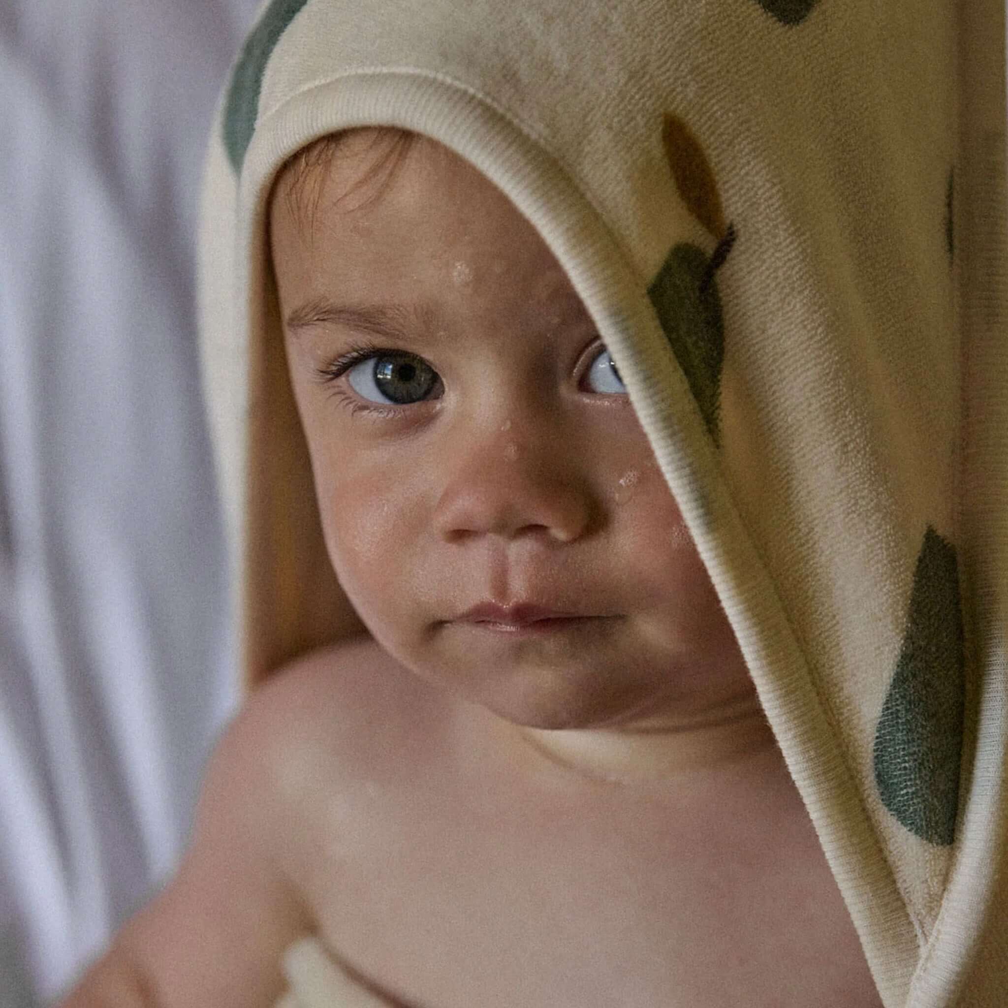 Baby wrapped in Nature Baby Organic Cotton Hooded Towel - Pear, featuring cute bear ears and soft organic cotton.