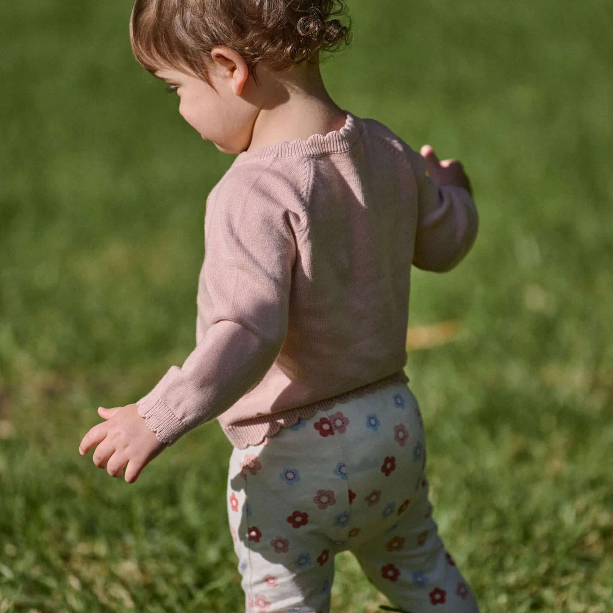 Nature Baby Organic Cotton Liliette Cardigan - Rose Dust worn by a child in a field, showcasing its soft design.