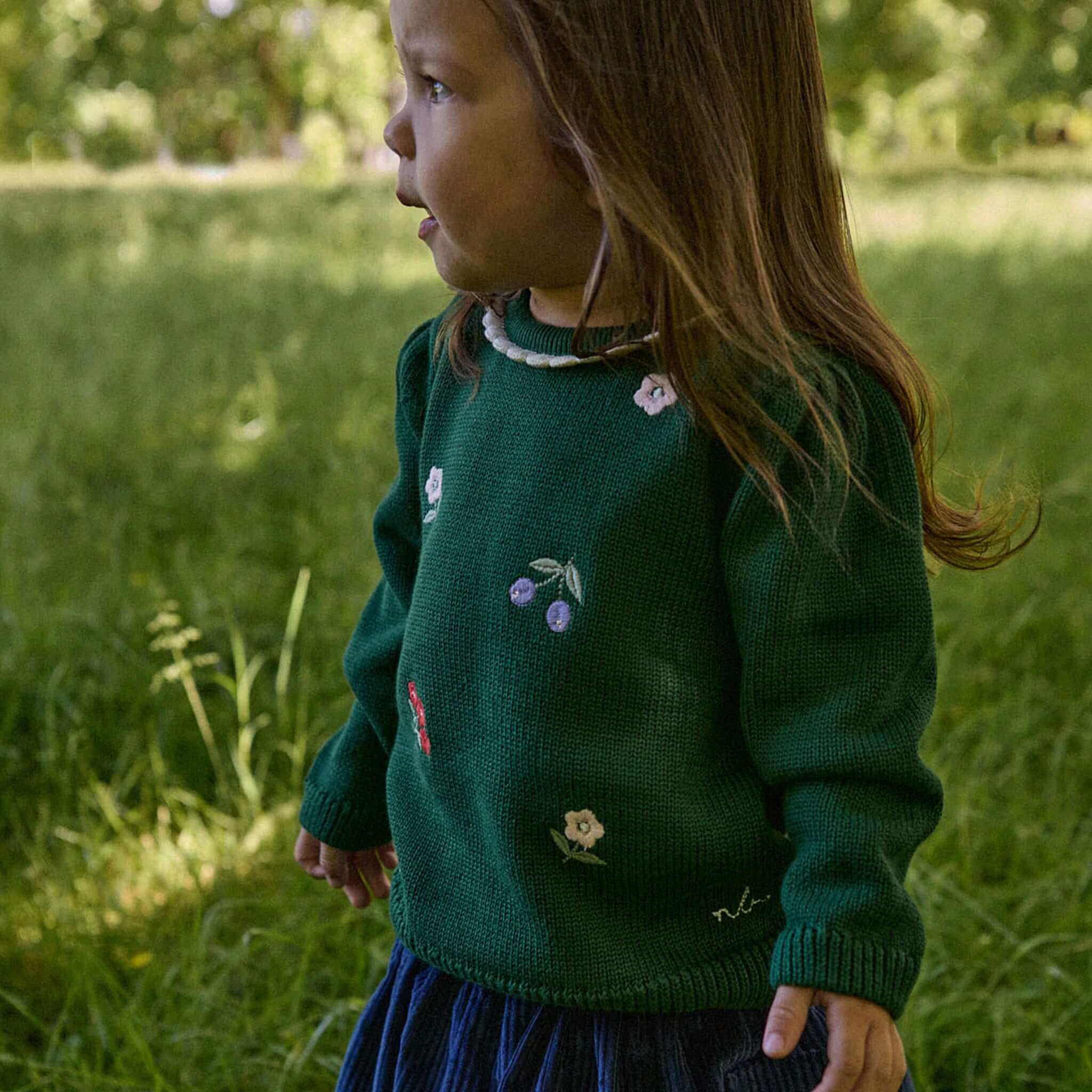 Alt Tag: Nature Baby Organic Cotton Margot Sweater - Eden Garden on child, green knit with floral embroidery and scalloped neckline outdoors
