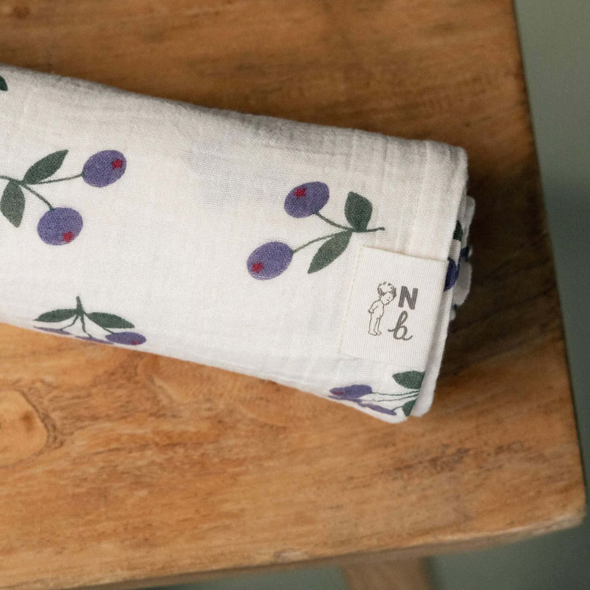 Alt Tag: Nature Baby Organic Cotton Muslin Wrap - Winter Berry Natural folded organic cotton muslin swaddle wrap with berry print