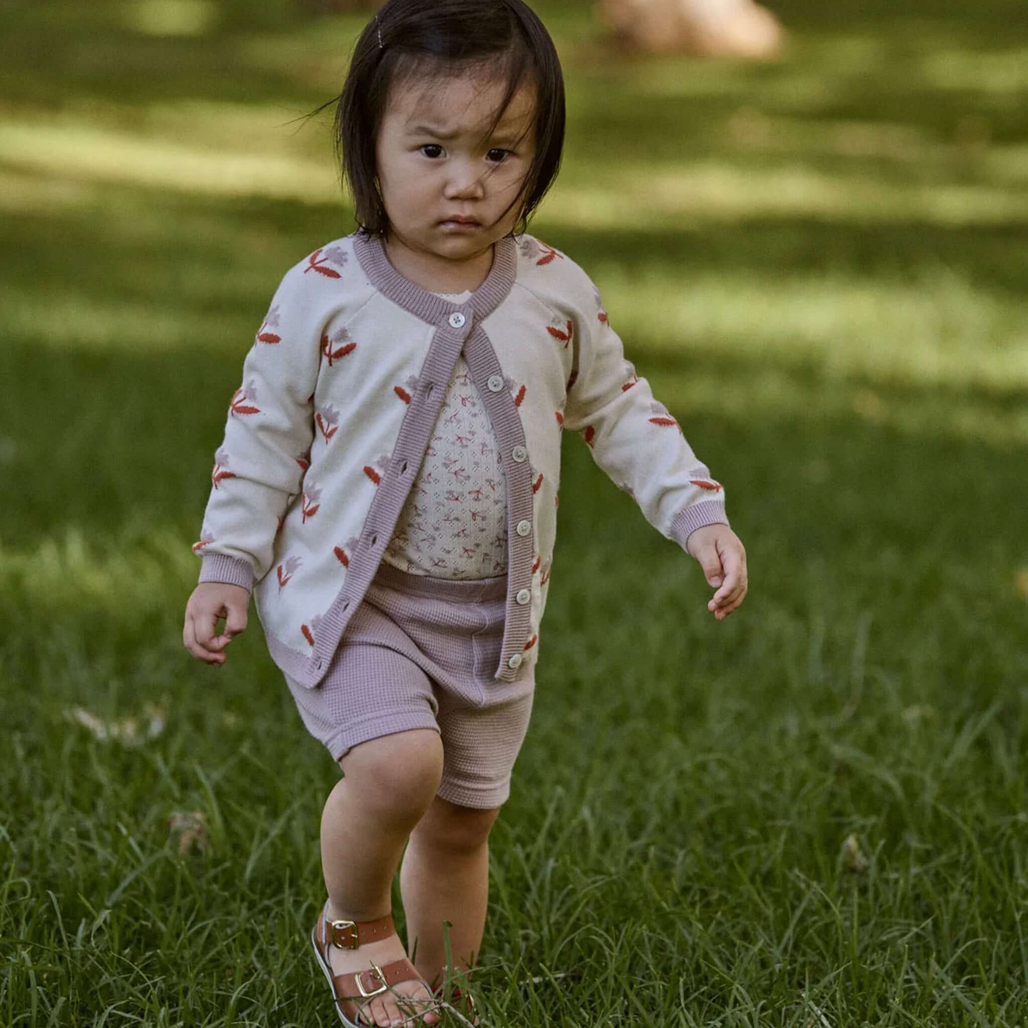 Nature Baby Organic Cotton Piper Cardigan - Fleurette worn by a child walking on grass in a park.