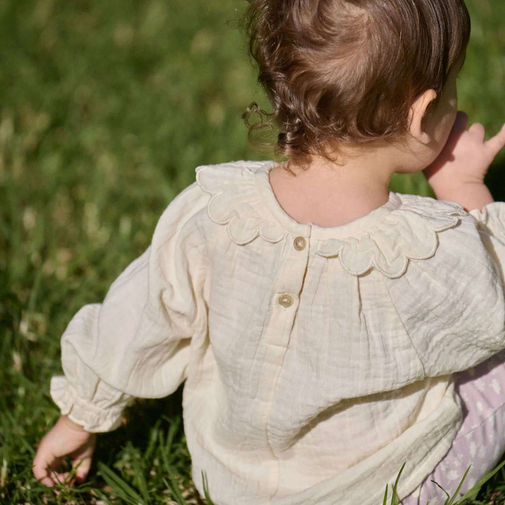 Nature Baby Organic Cotton Ruffle Cameron Blouse - Natural on a child outdoors in a grassy field.
