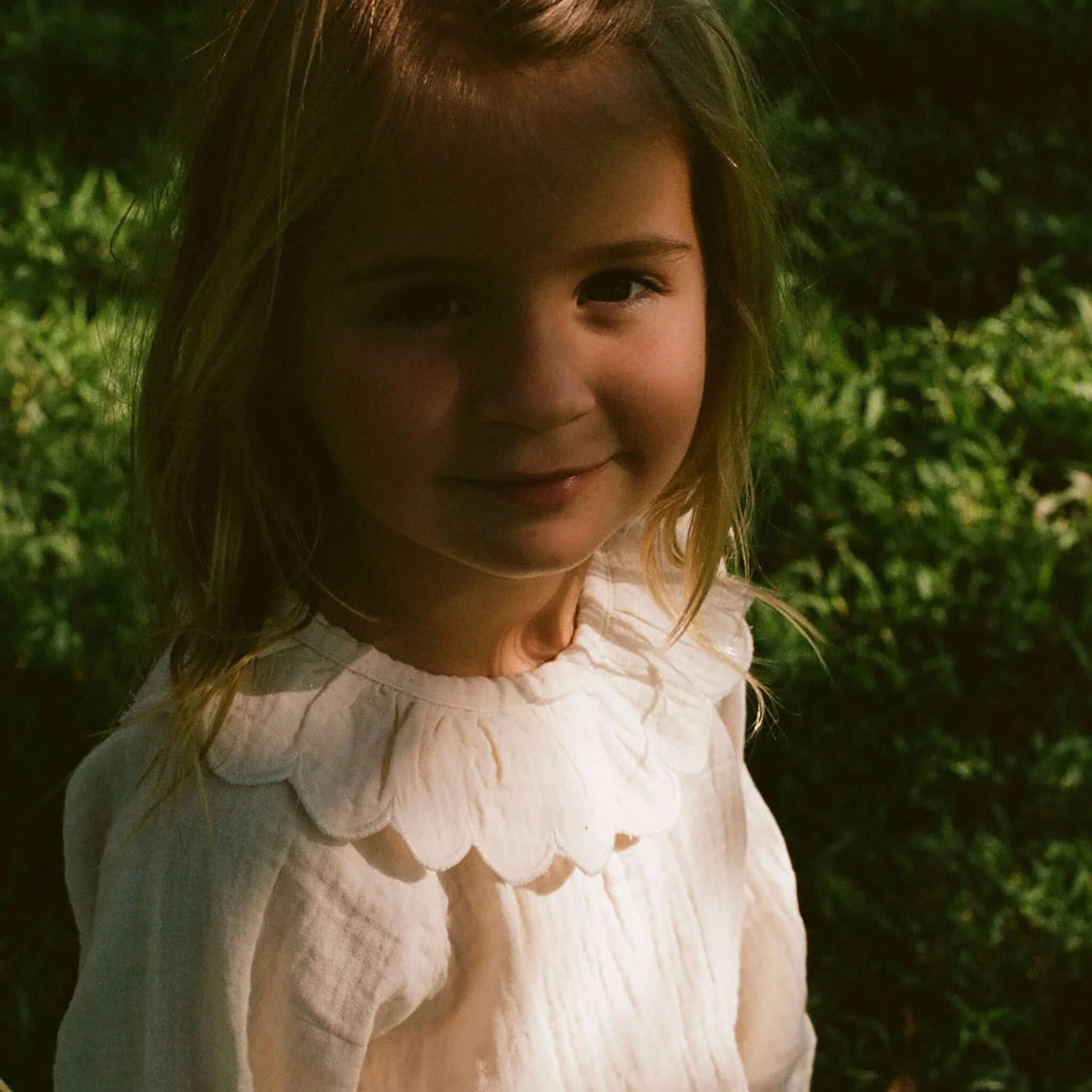 Nature Baby Organic Cotton Ruffle Cameron Blouse - Natural worn by a young girl outdoors with a soft ruffle collar.