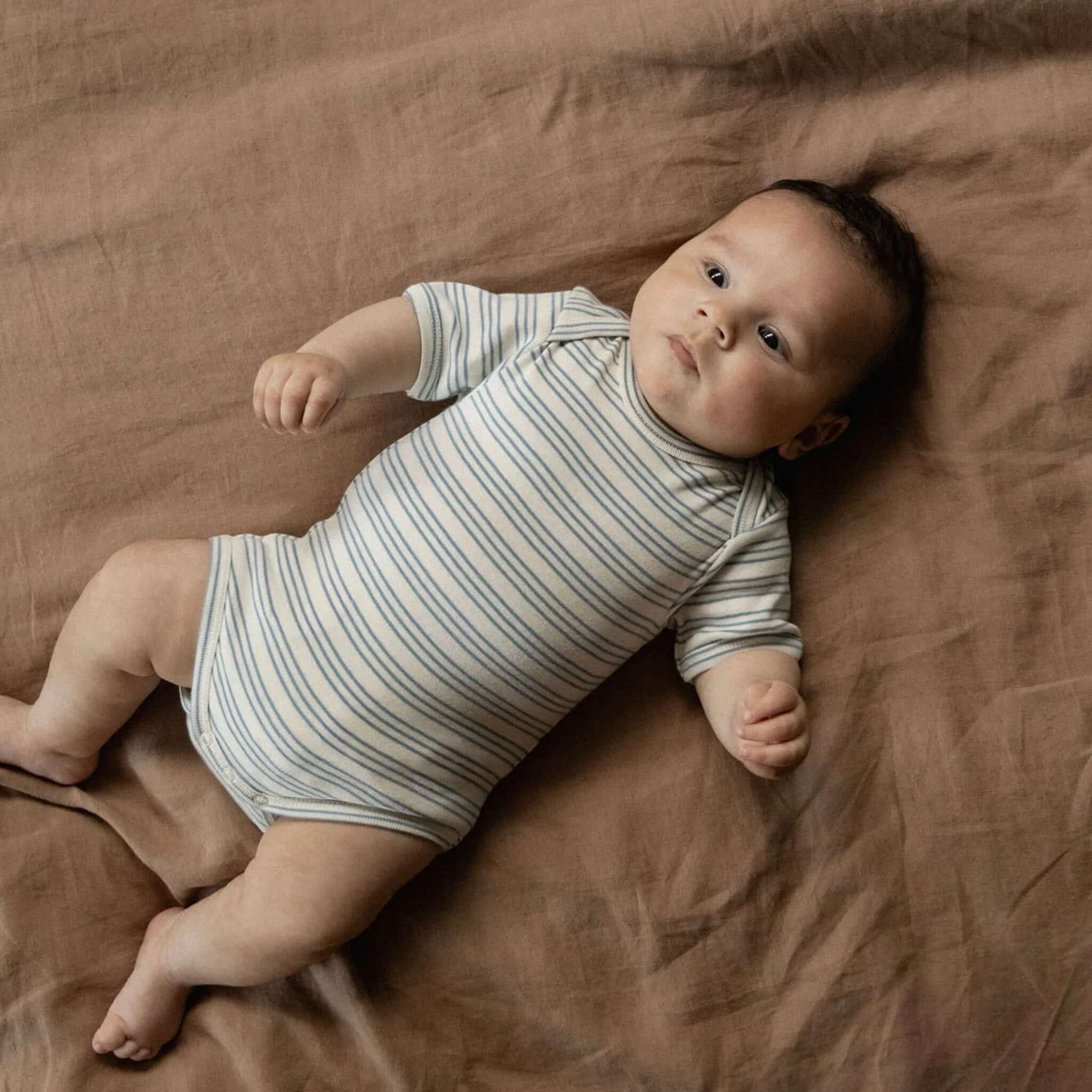 Nature Baby Organic Cotton Short Sleeve Bodysuit - Stripe Trio on a baby resting on a soft blanket.