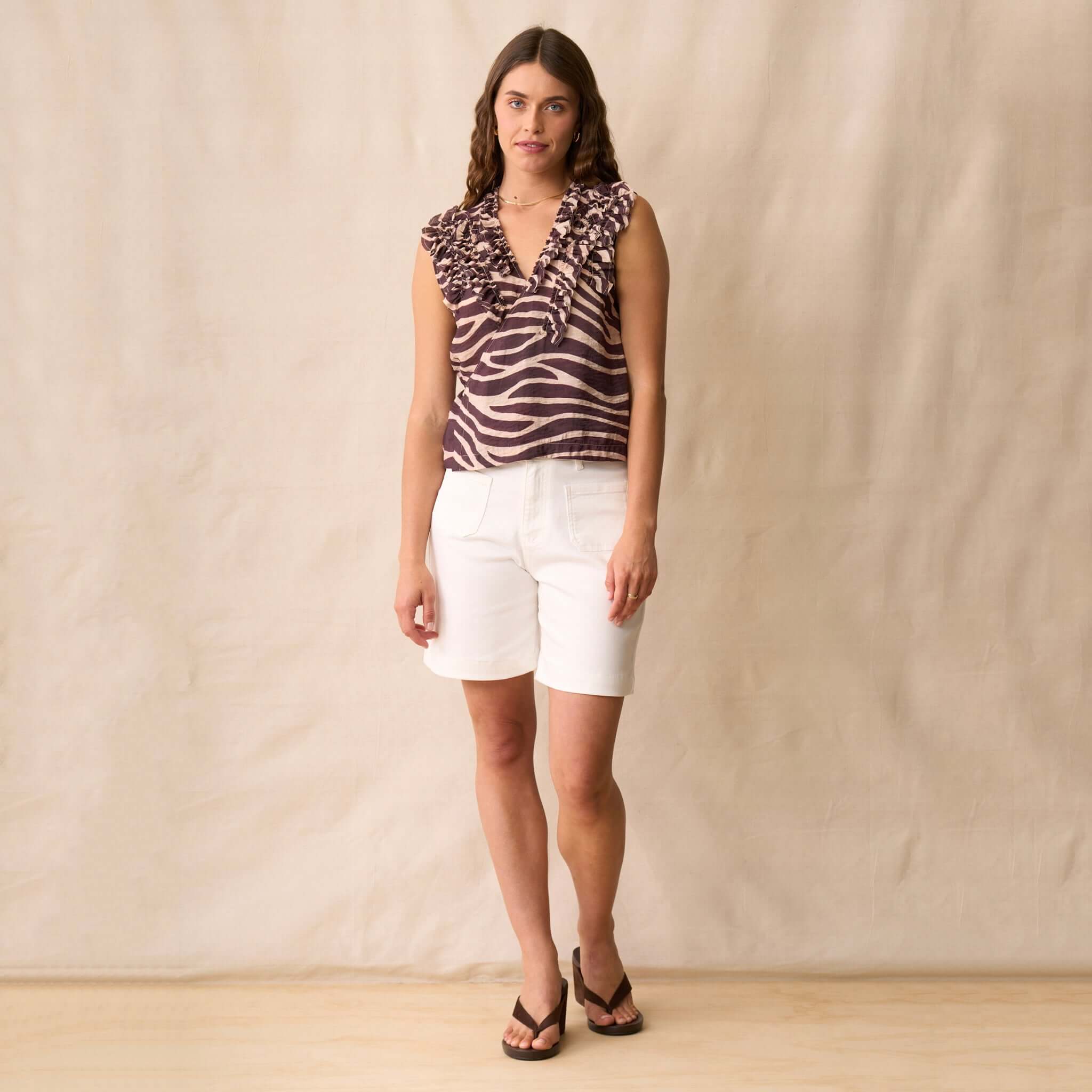 Neris Dazzle Shirt - Mahogany worn by a model with white shorts, showcasing its cropped wrap style and zebra print.