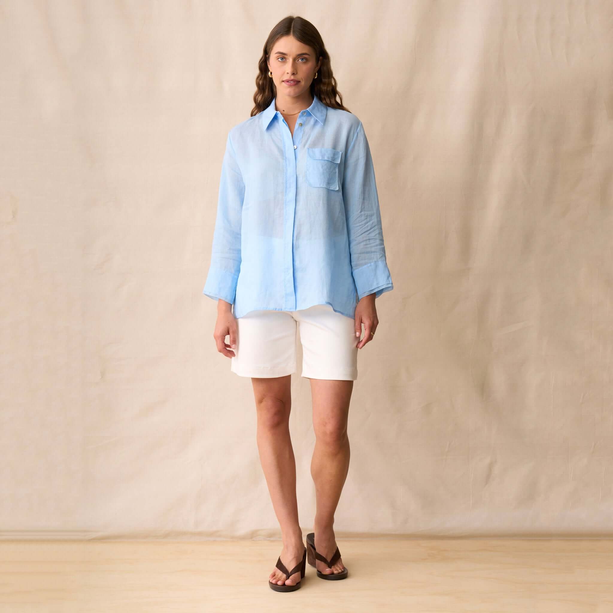 Woman wearing the Neris Drew Shirt - Skye in soft blue, paired with white shorts, showcasing a relaxed summer style.