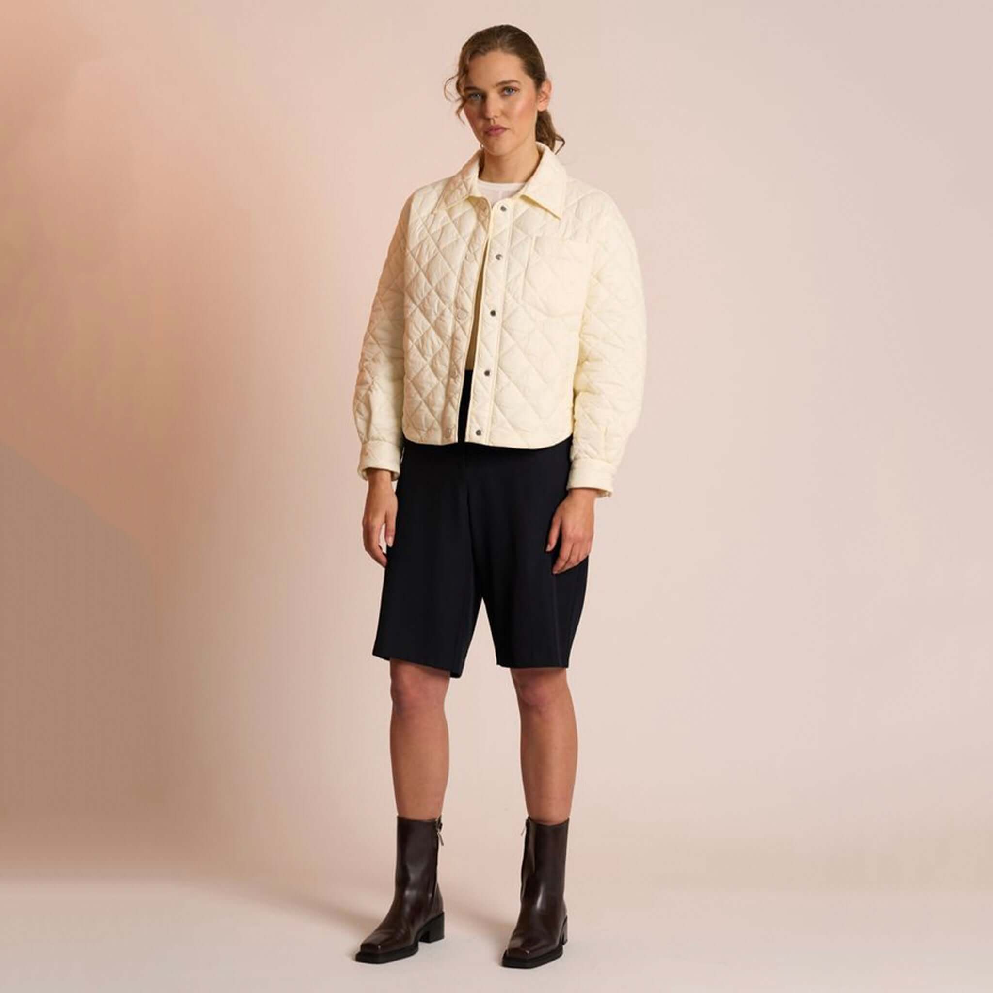 Alt Tag: Neris Gia Jacket - Egret quilted cropped cream jacket with snap domes and collar, styled over black shorts and ankle boots