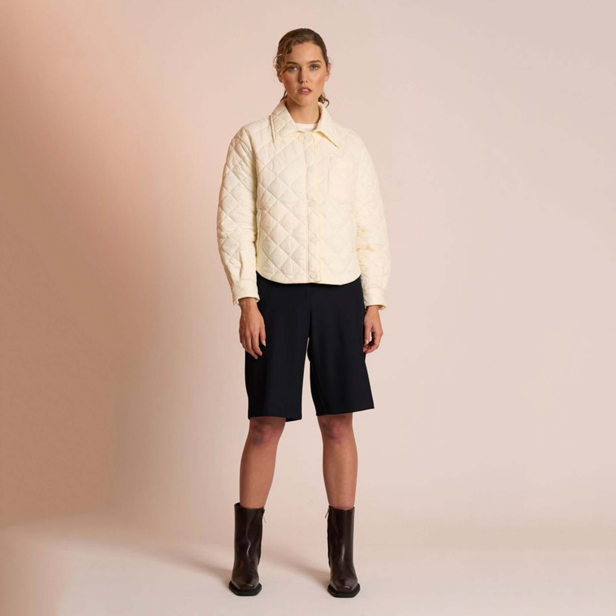 Alt Tag: Neris Gia Jacket - Egret quilted cropped jacket in soft cream with snap domes and structured collar, styled with black shorts