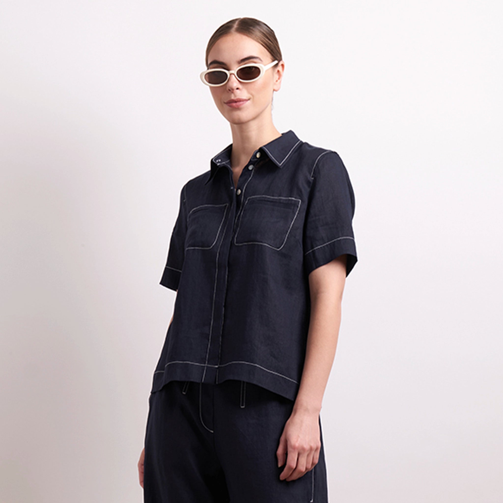 Woman wearing a dark denim shirt and sunglasses on a light background