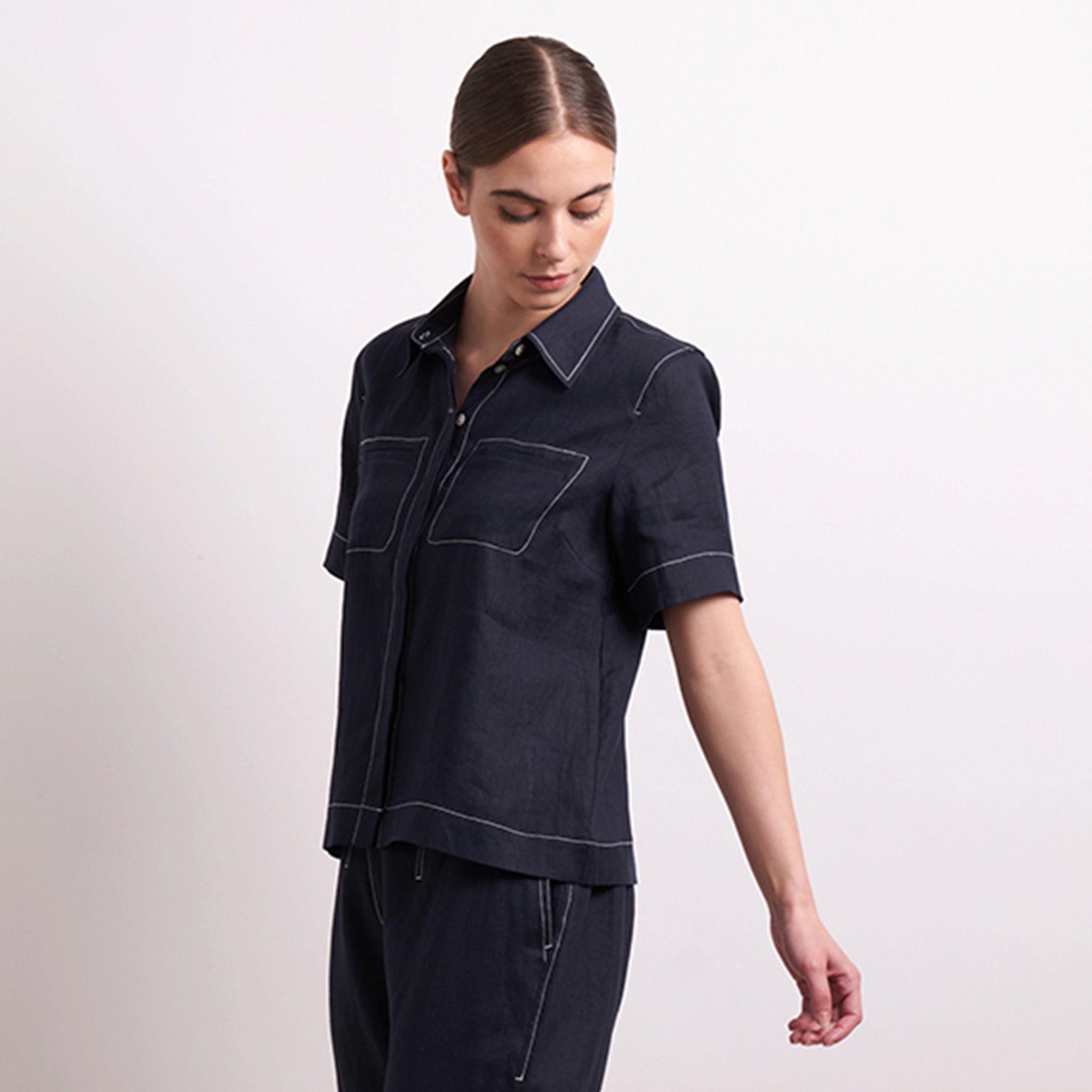 Woman wearing a dark denim shirt and pants on a light background