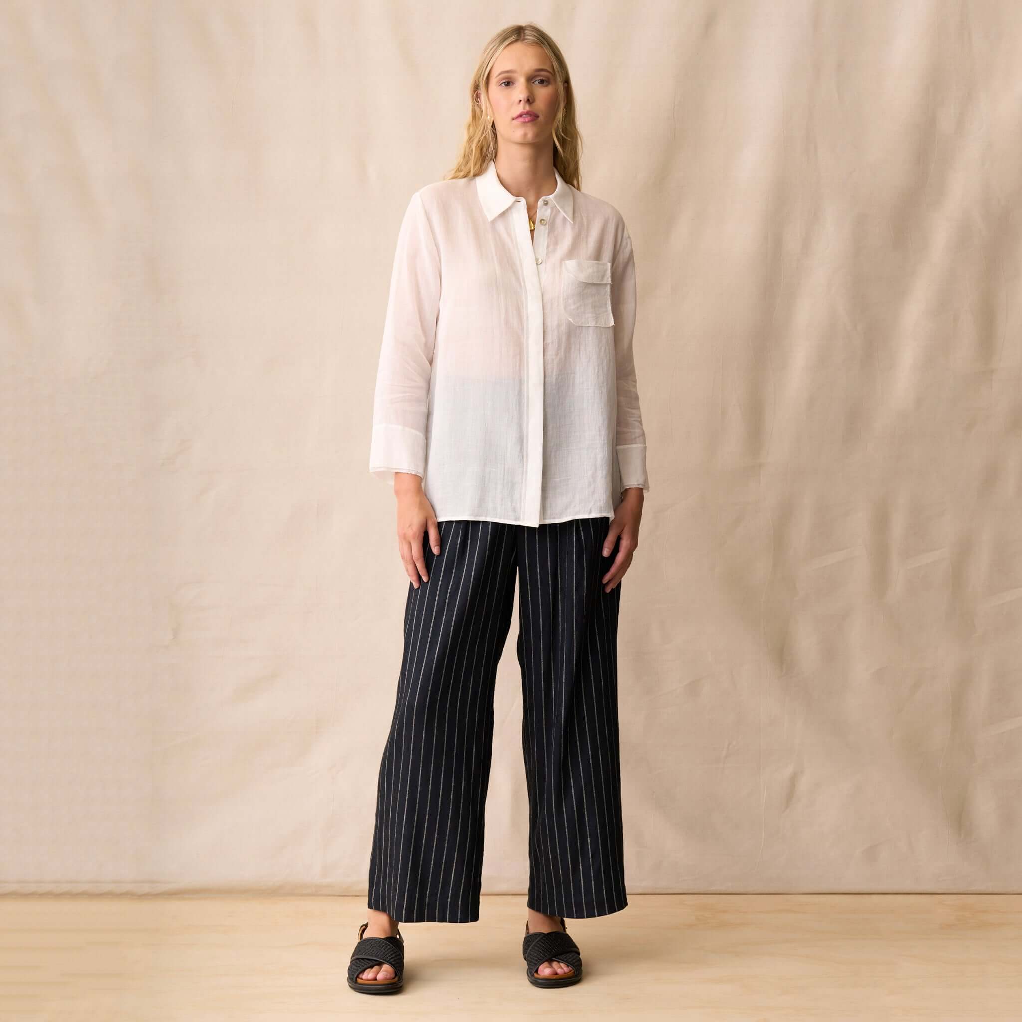 Neris Phoebe Top - White worn with striped pants on a model, showcasing its sheer and polished design.