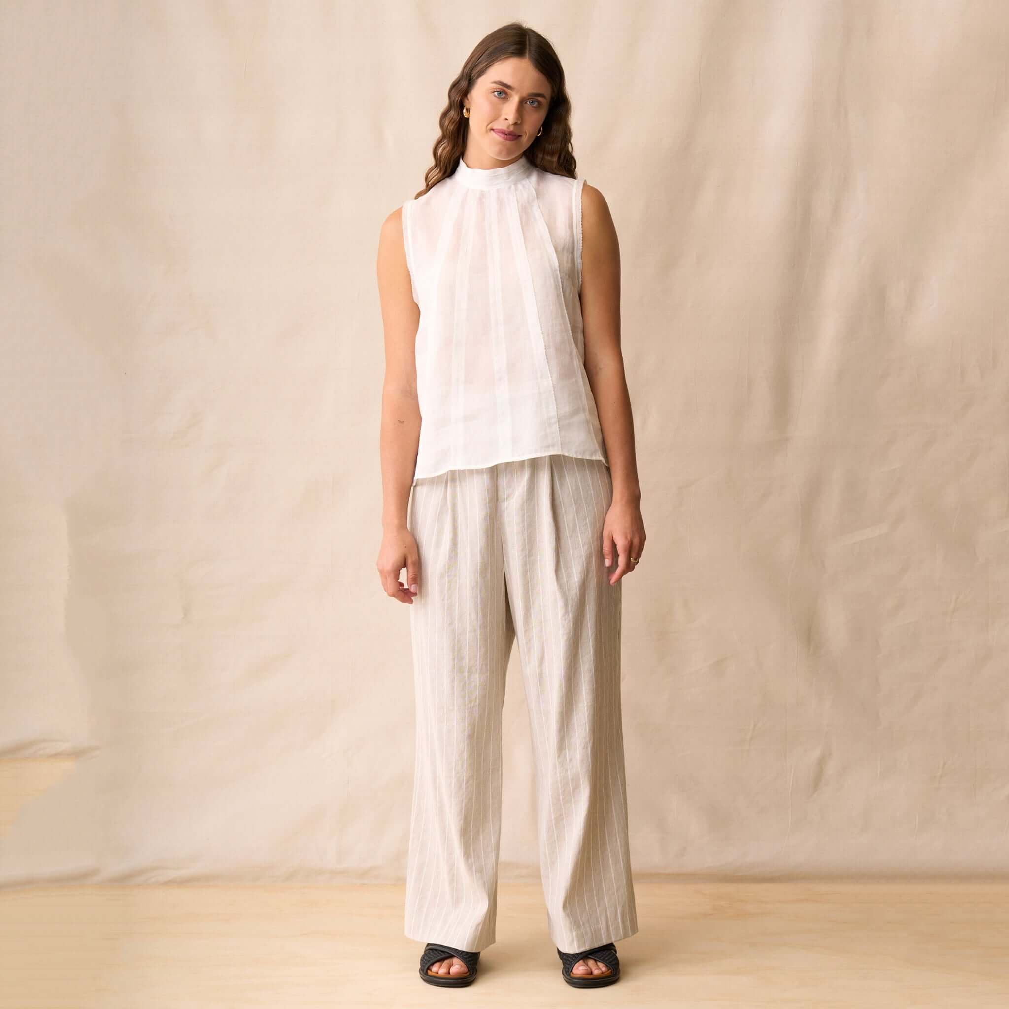 Neris Phoebe Top - White worn with light striped pants, showcasing a sleeveless, pleated design suitable for warm weather.