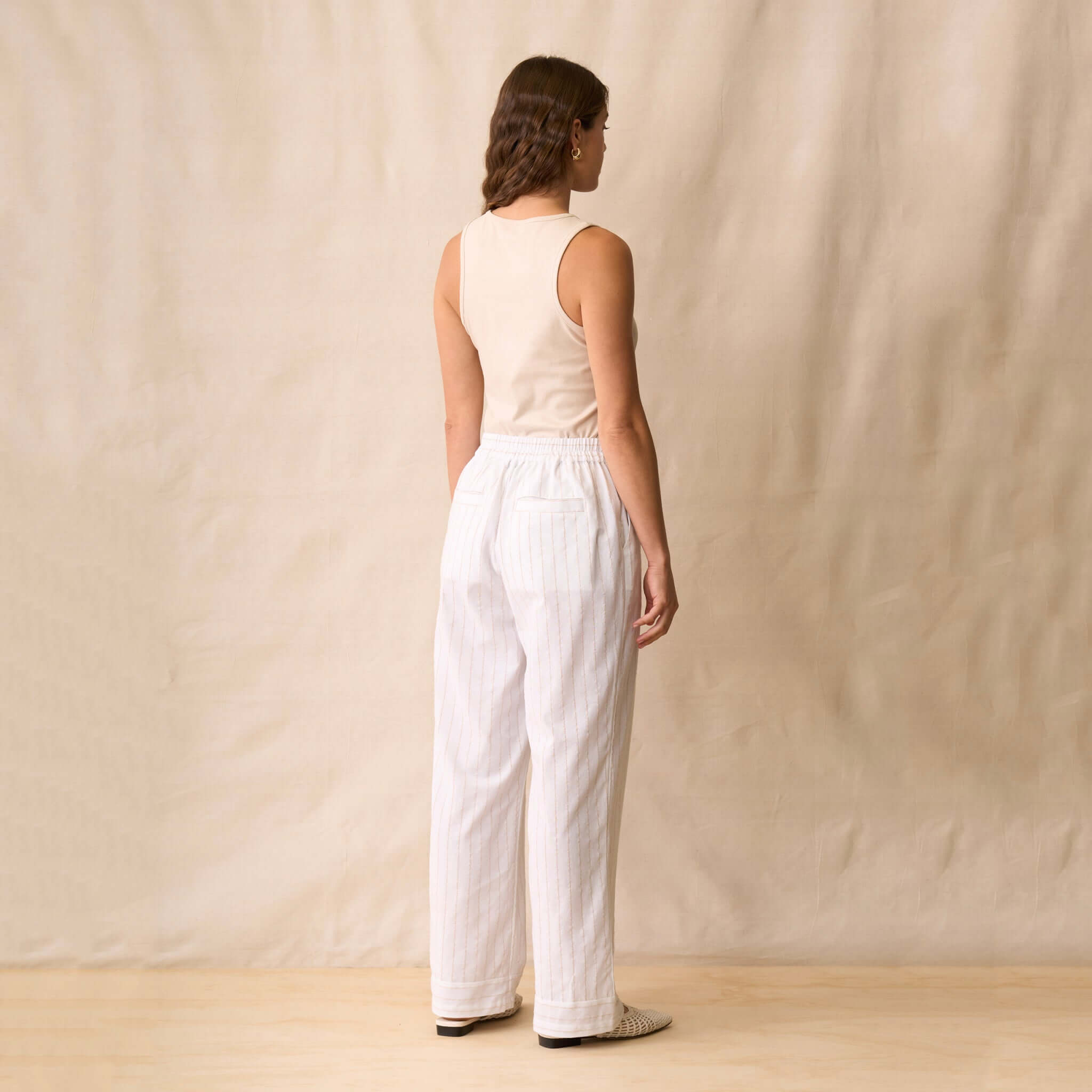 Neris Ziggy Tank - Sand worn with wide-leg striped pants, showcasing a stylish back view against a neutral background.