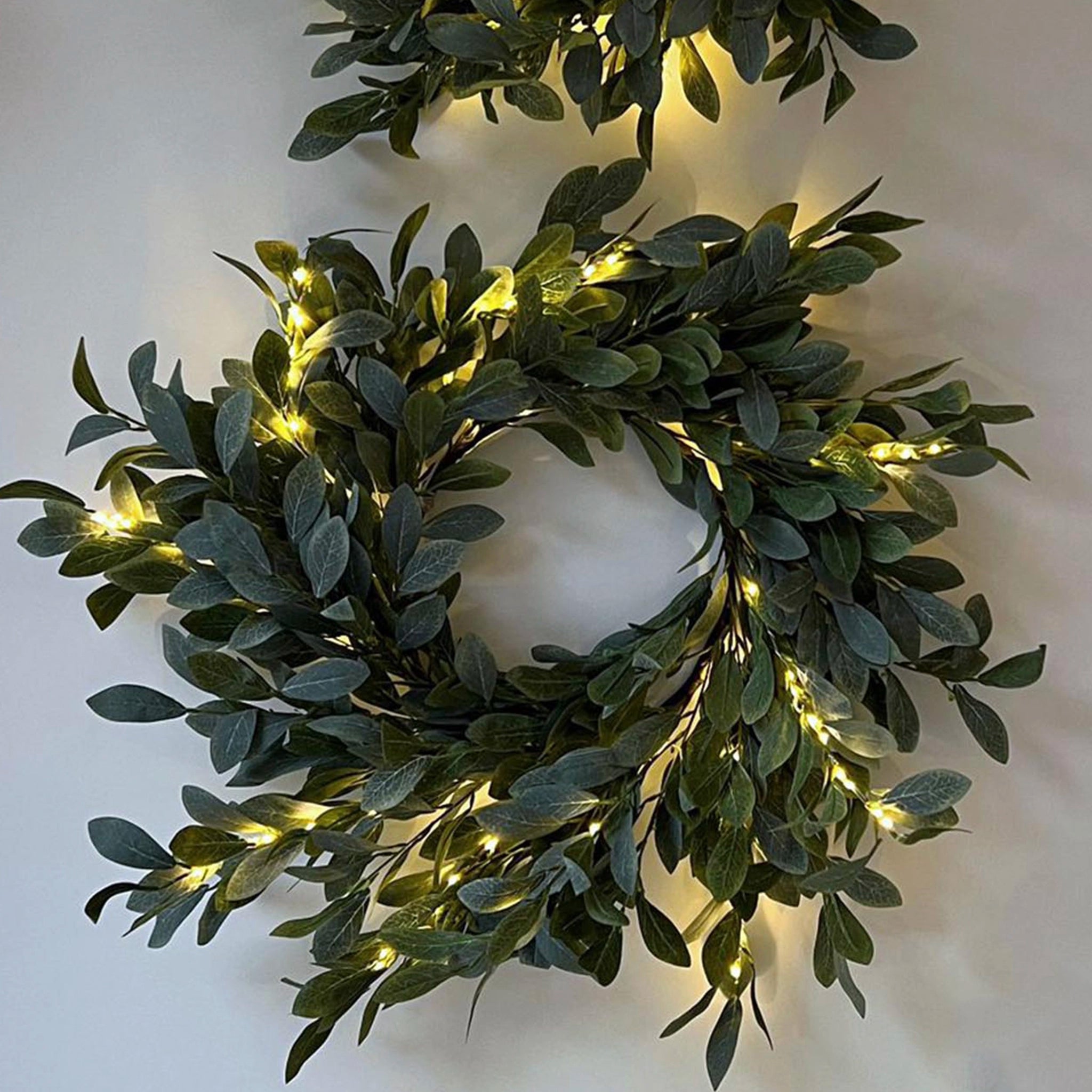 Decorative wreath with green leaves and embedded lights on a white background