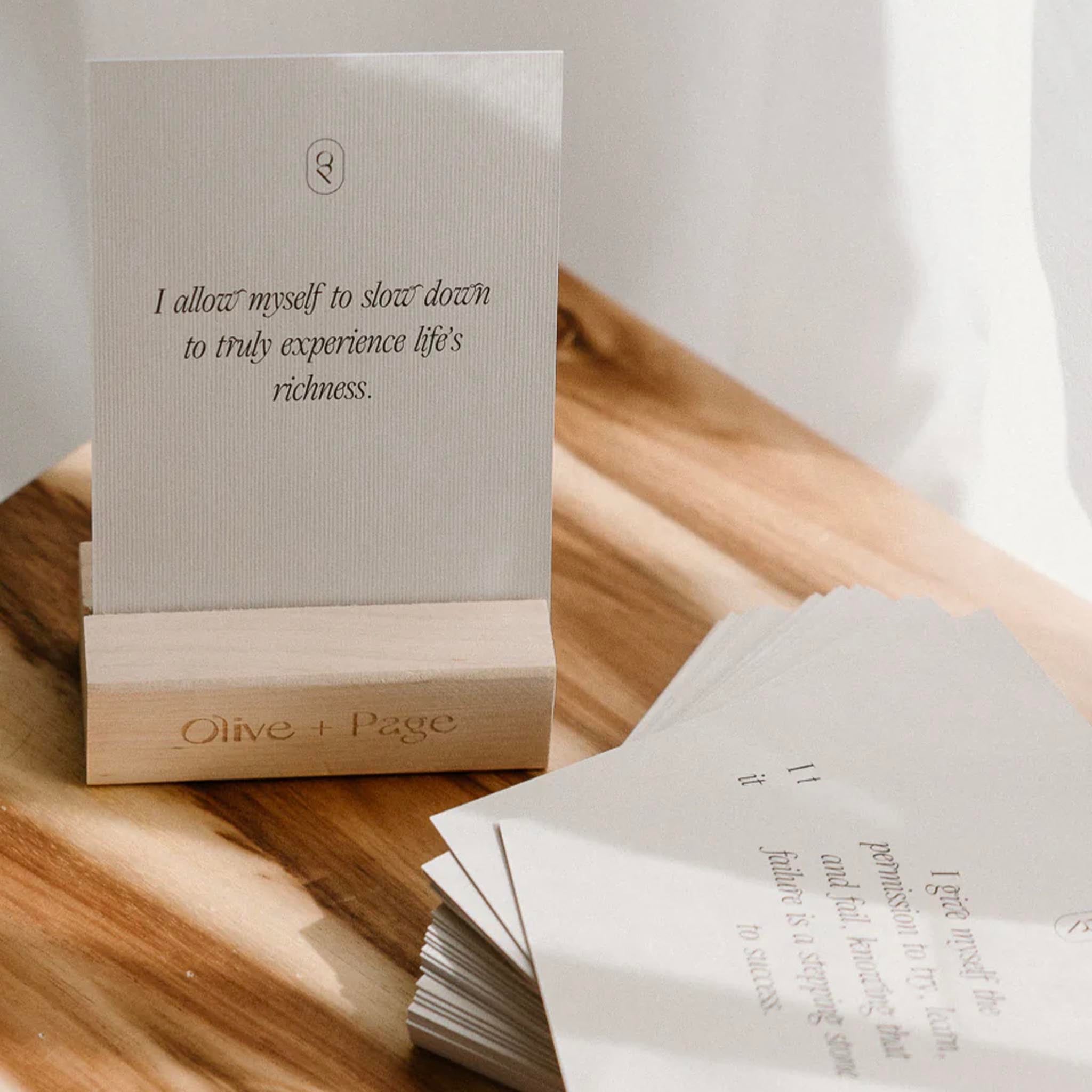 Card with text on a wooden stand with 'Olive + Page' branding, placed on a wooden surface.