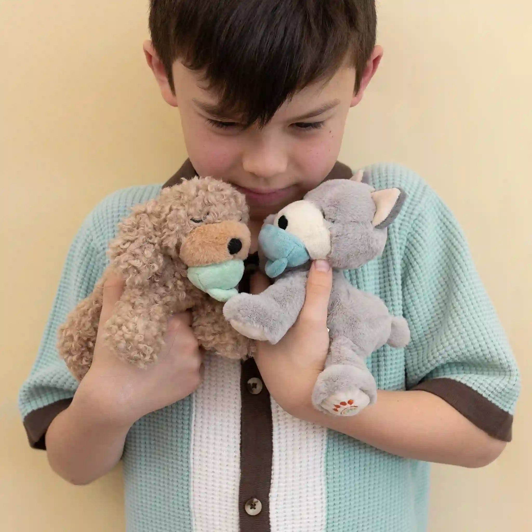 Child holding two plush toys against a plain background