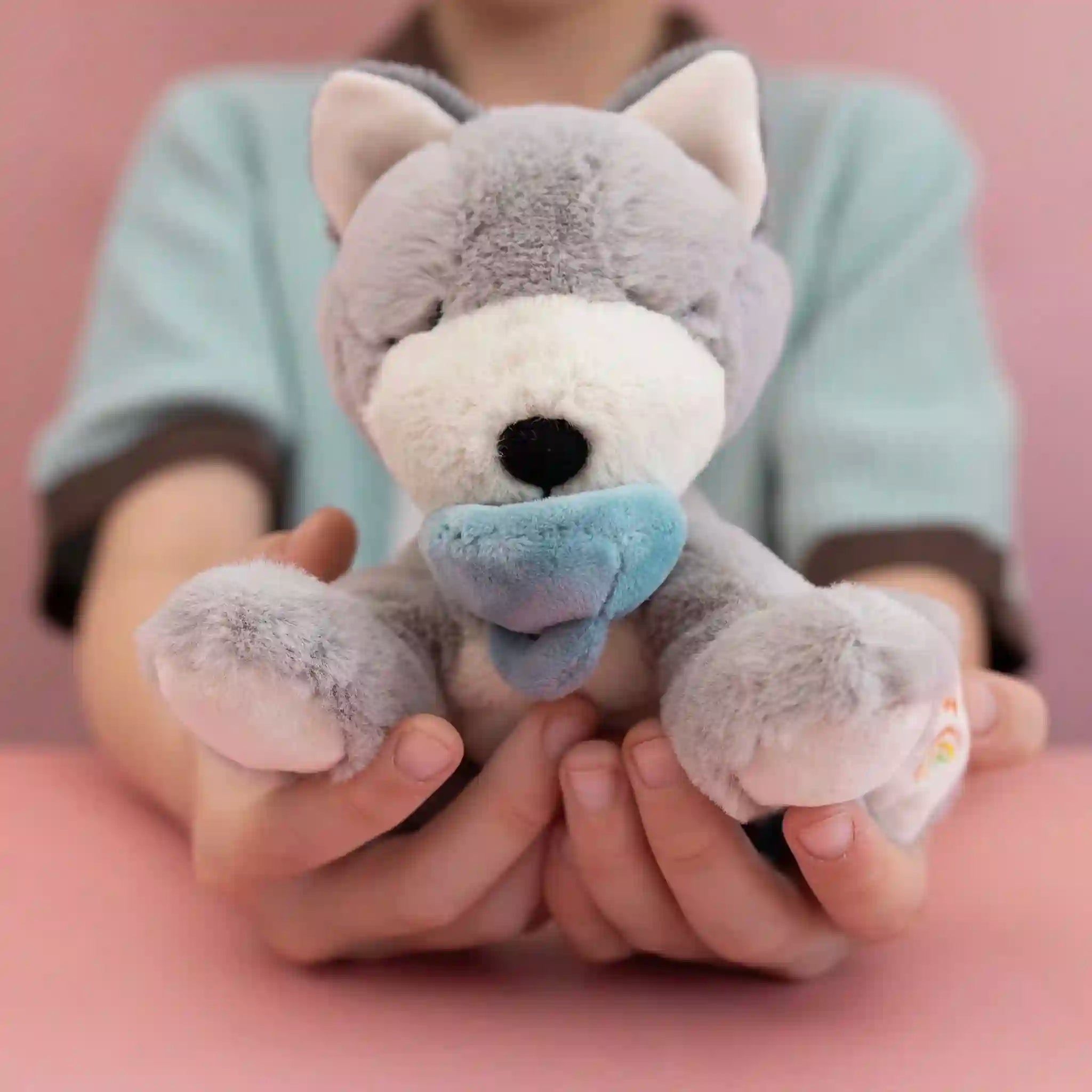 Person holding a plush toy in their hands against a pink background