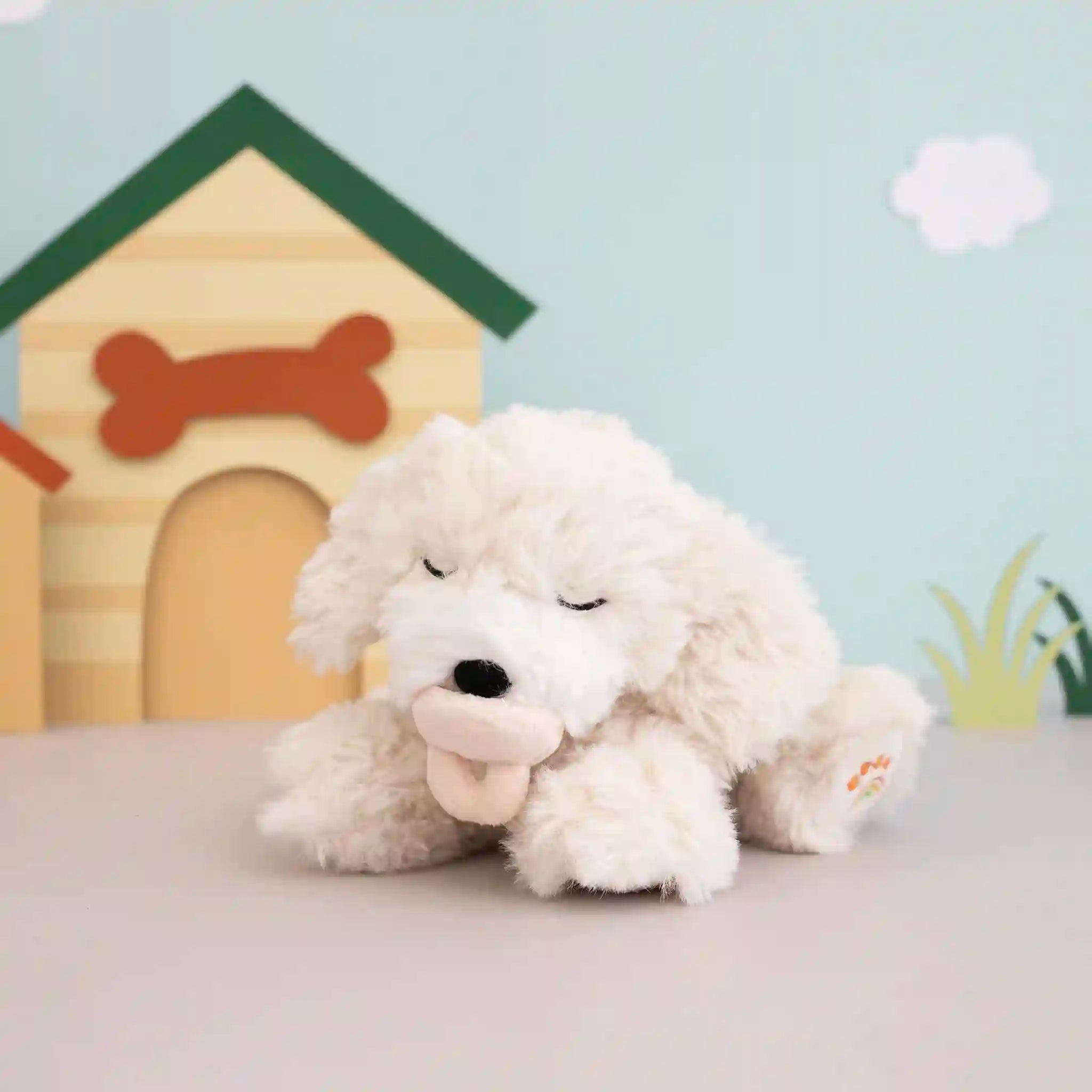 White plush dog toy with a bone in its mouth, sitting in front of a wooden doghouse with a bone on a light blue background.