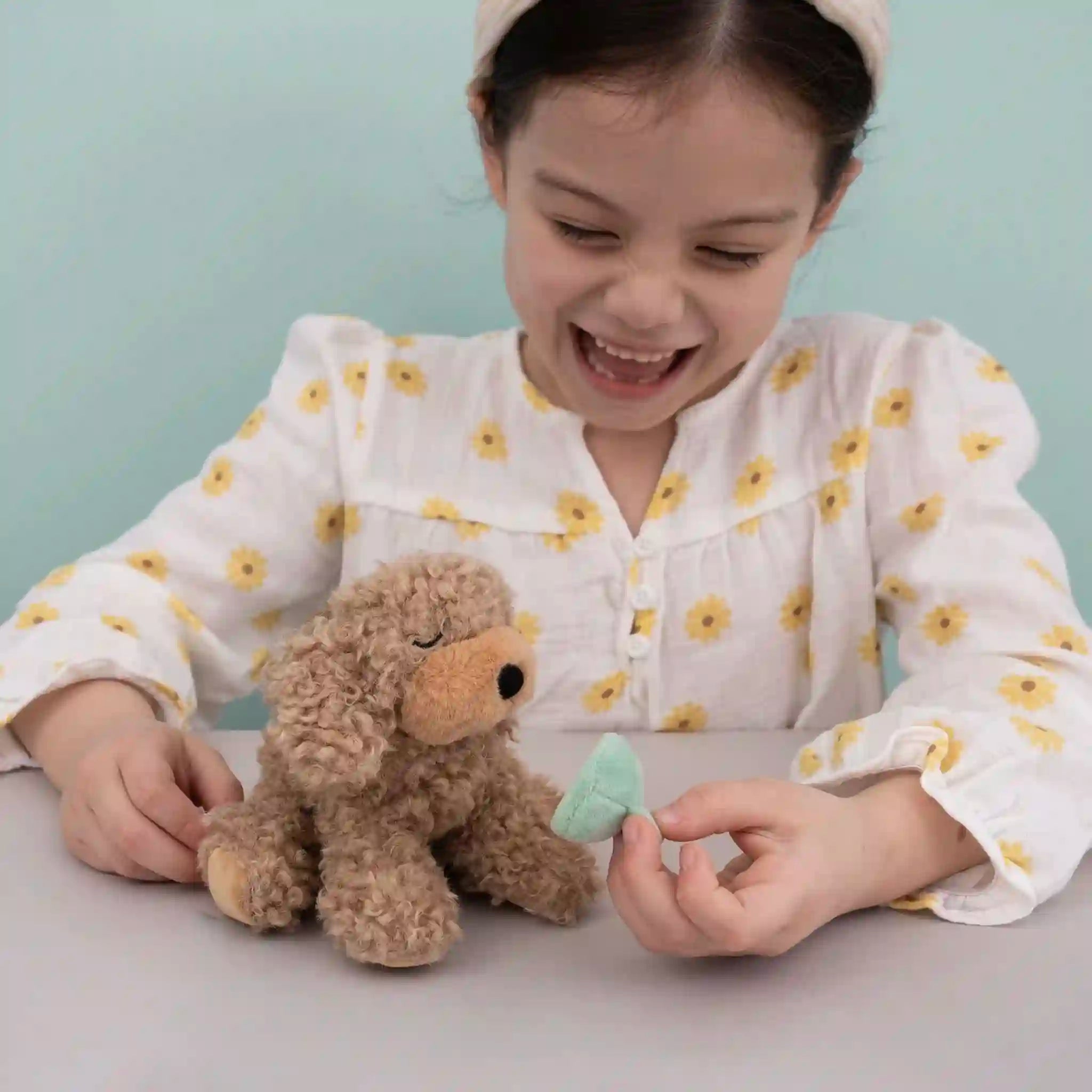 Child playing with a plush toy and a green object on a light blue background