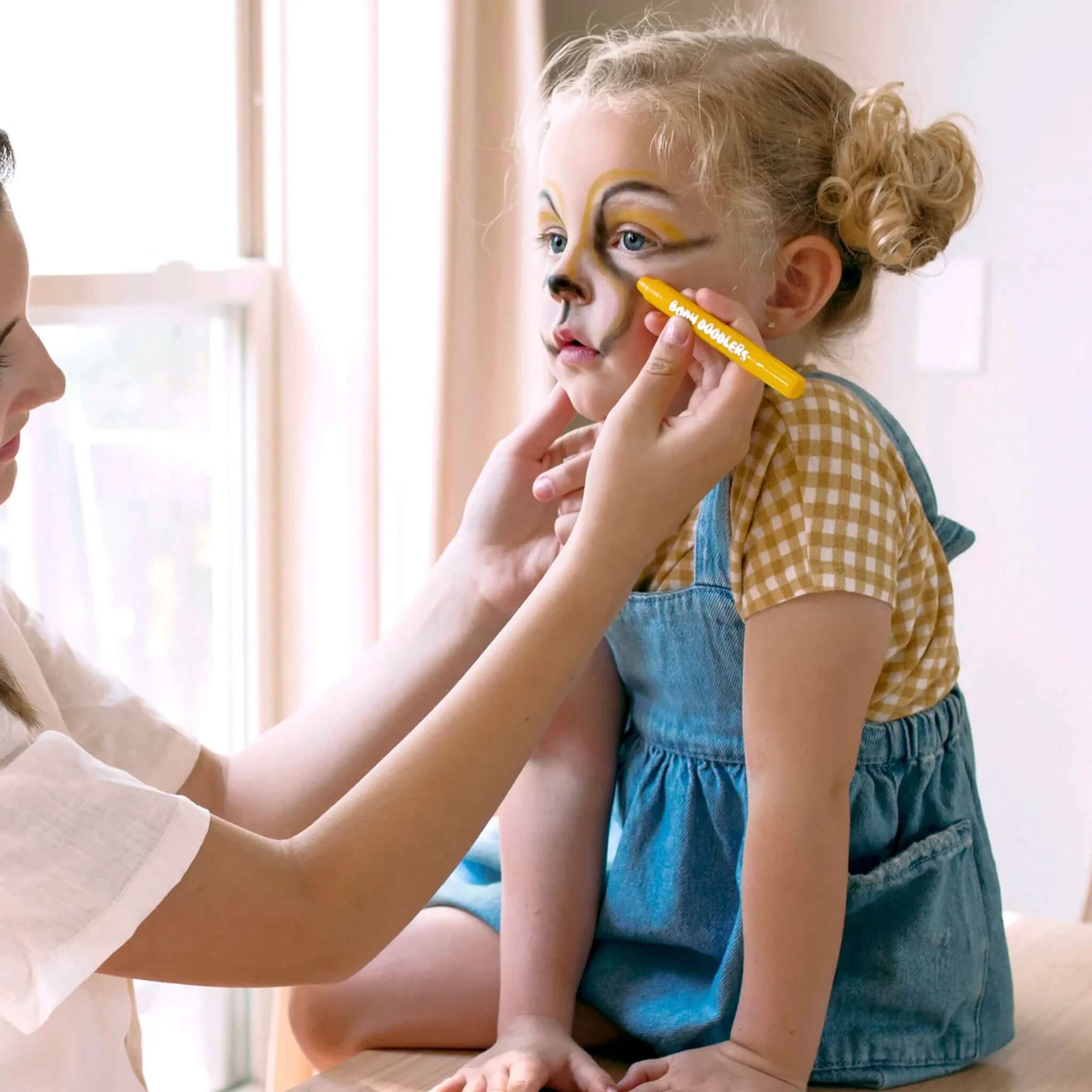 A child being creatively painted with Ooly Face & Body Doodlers Crayons, transforming into a playful character.