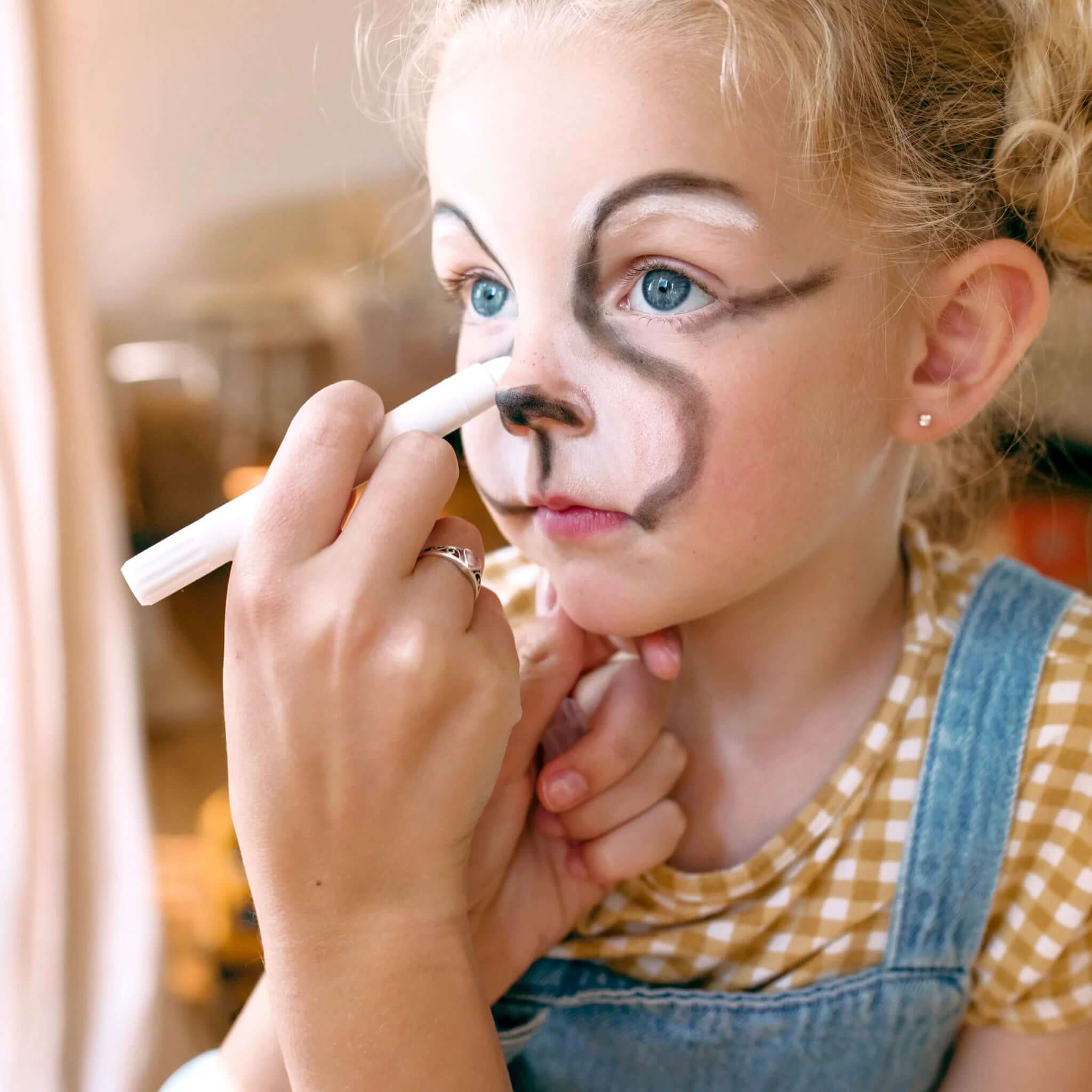 A child getting face painting with Ooly Face & Body Doodlers Crayons, transforming into a playful character.