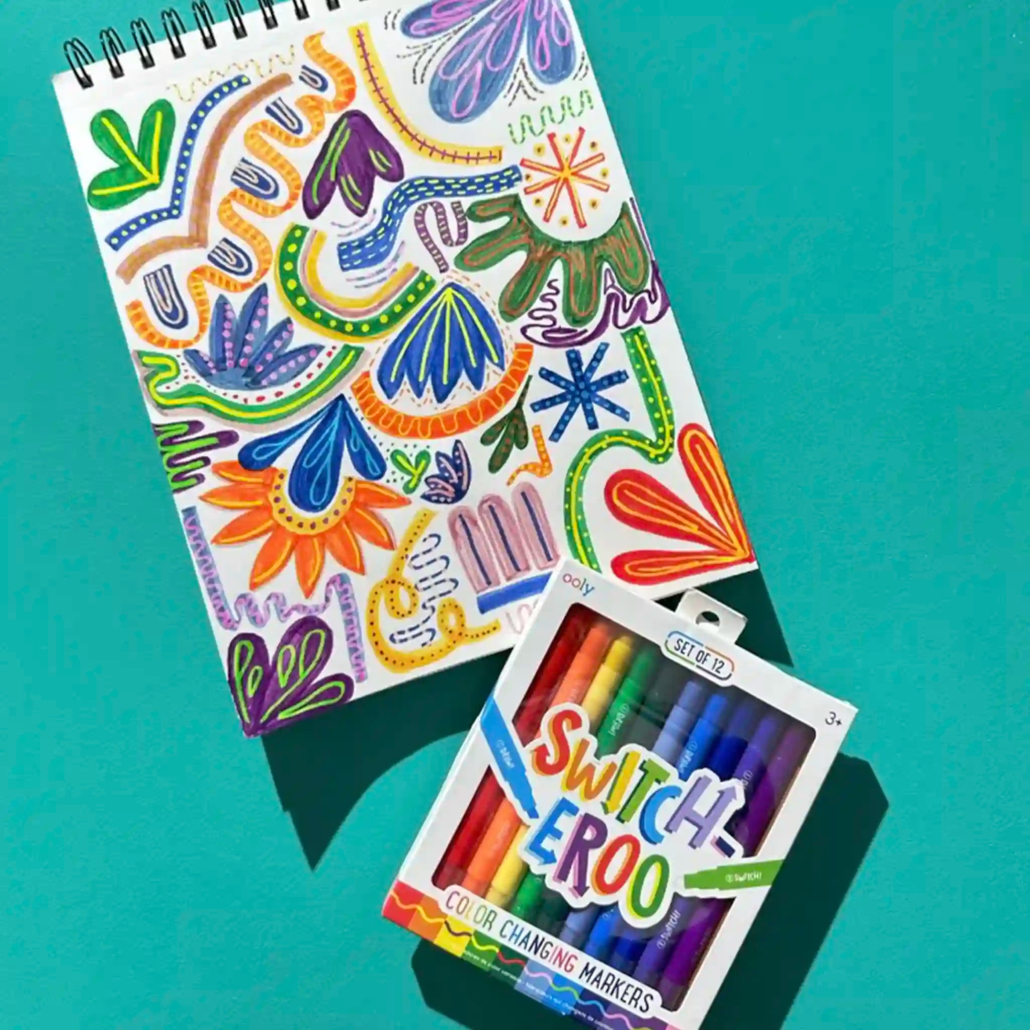 Colorful notebook with floral designs and a set of Switch Eeroo markers on a teal background
