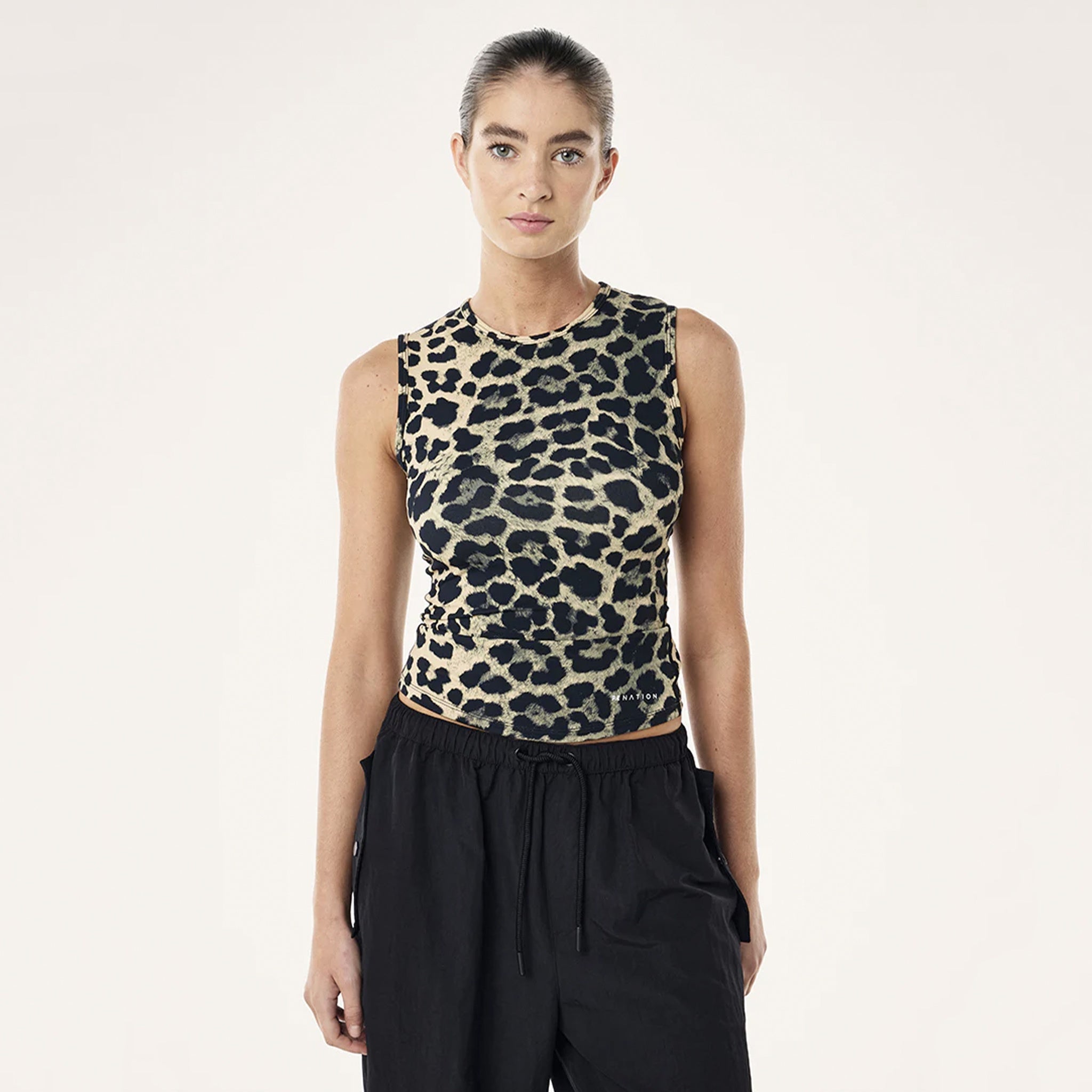 Person wearing a leopard print sleeveless top and black pants on a white background