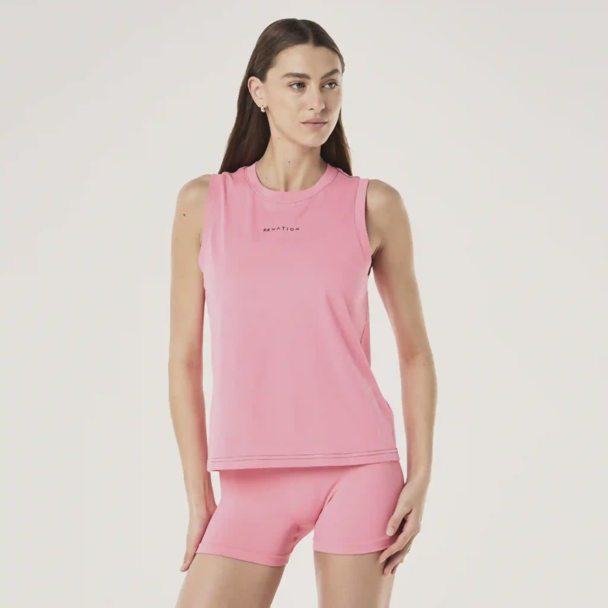 Woman wearing a pink sleeveless top and shorts set on a light gray background