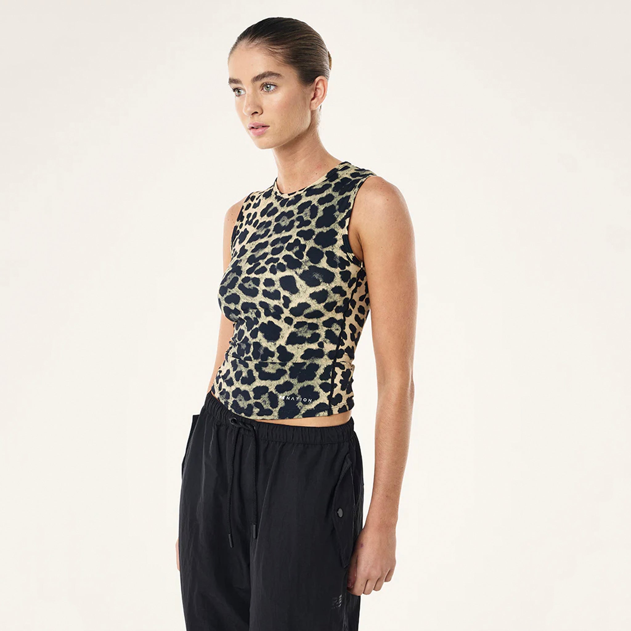 Woman wearing a leopard print sleeveless top and black pants on a light gray background