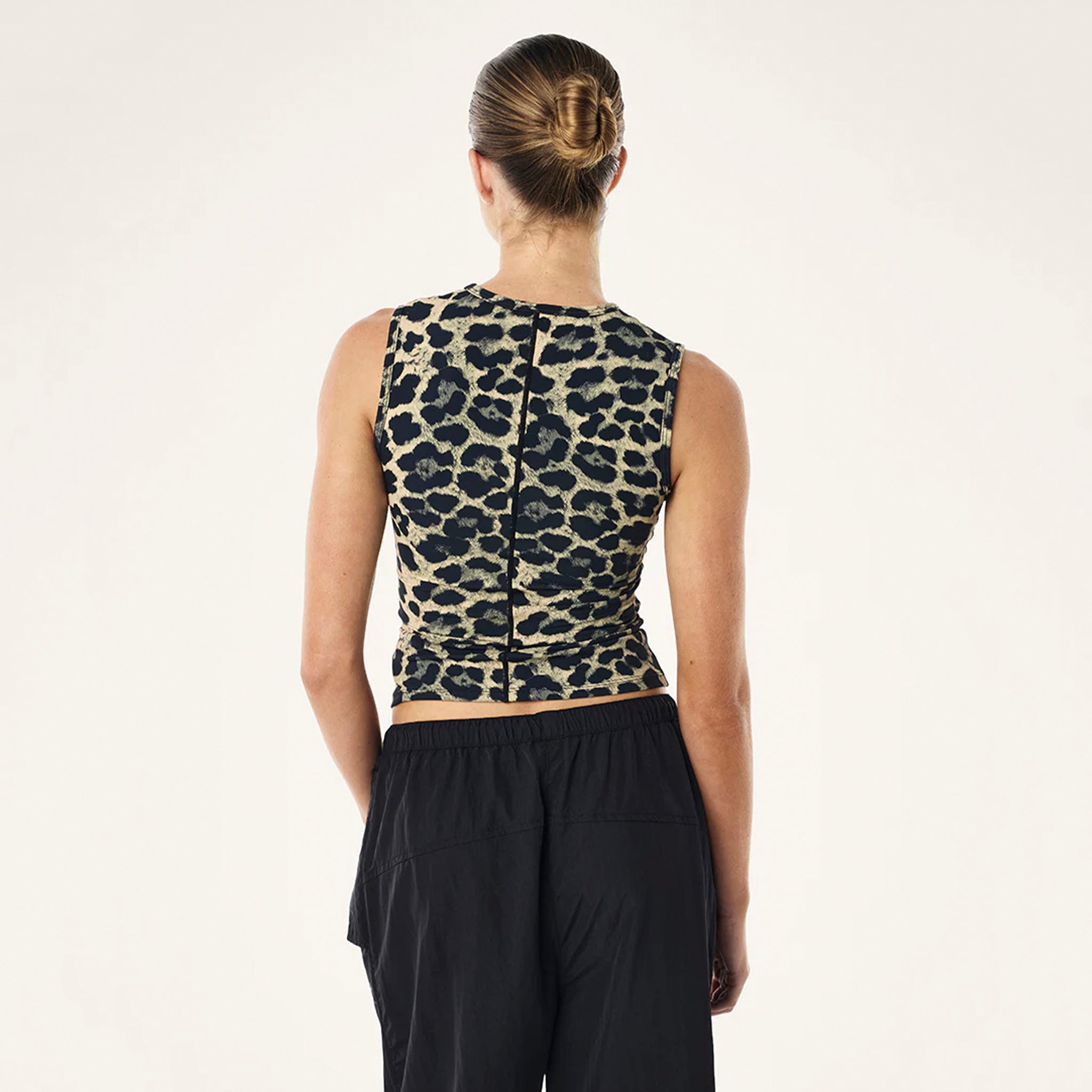 Person wearing a leopard print sleeveless top and black pants on a white background