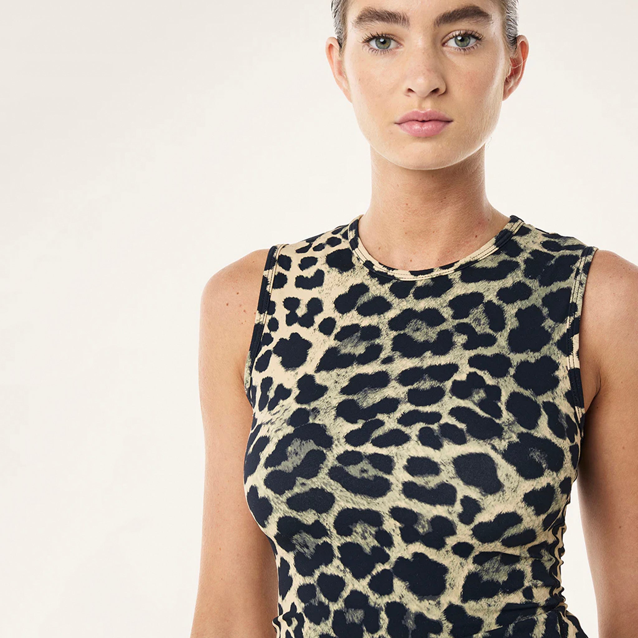 Person wearing a sleeveless top with a leopard print pattern on a plain background